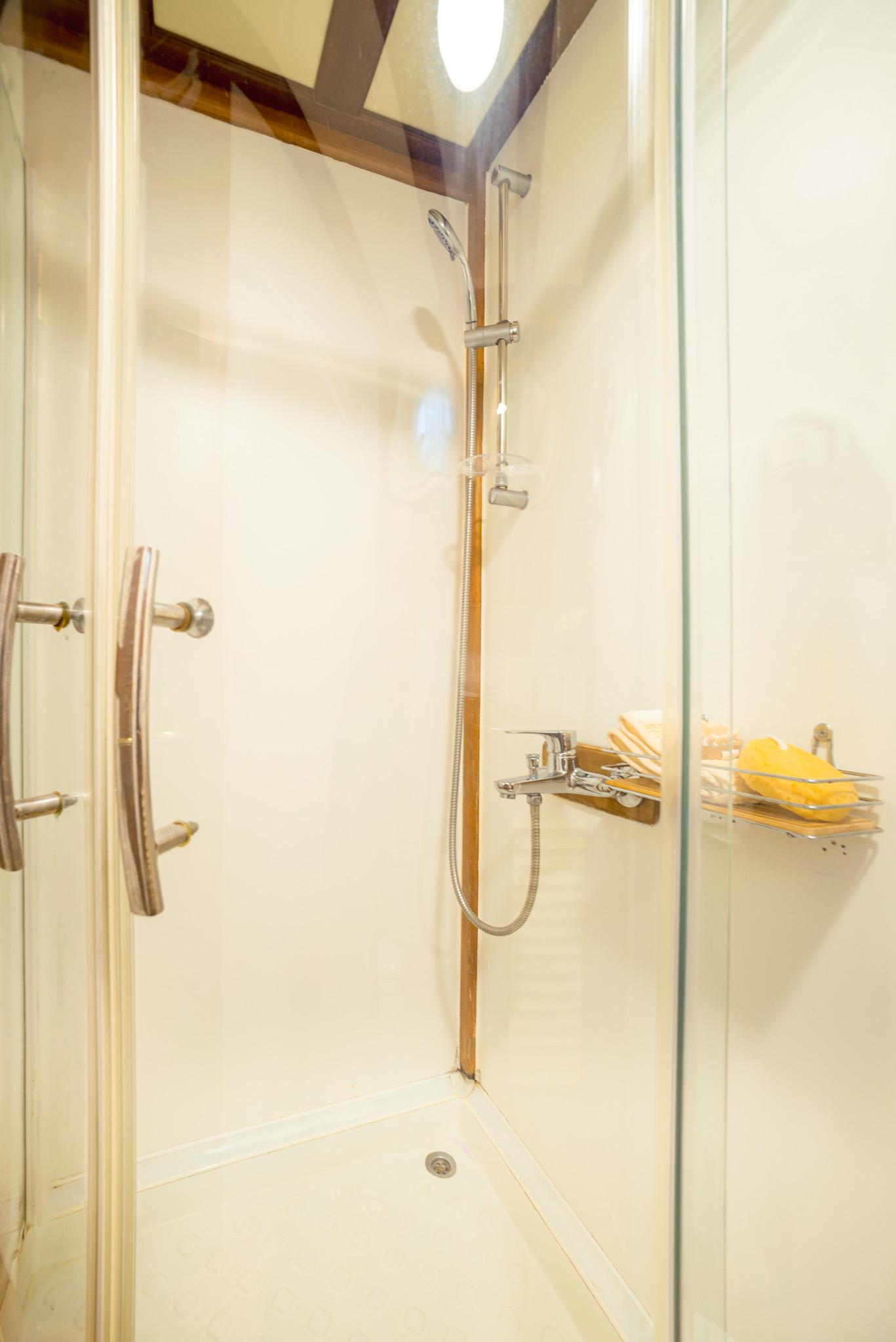 Enclosed glass shower cubicle with chrome handheld showerhead on sliding rail and teak trim in gulet cabin bathroom