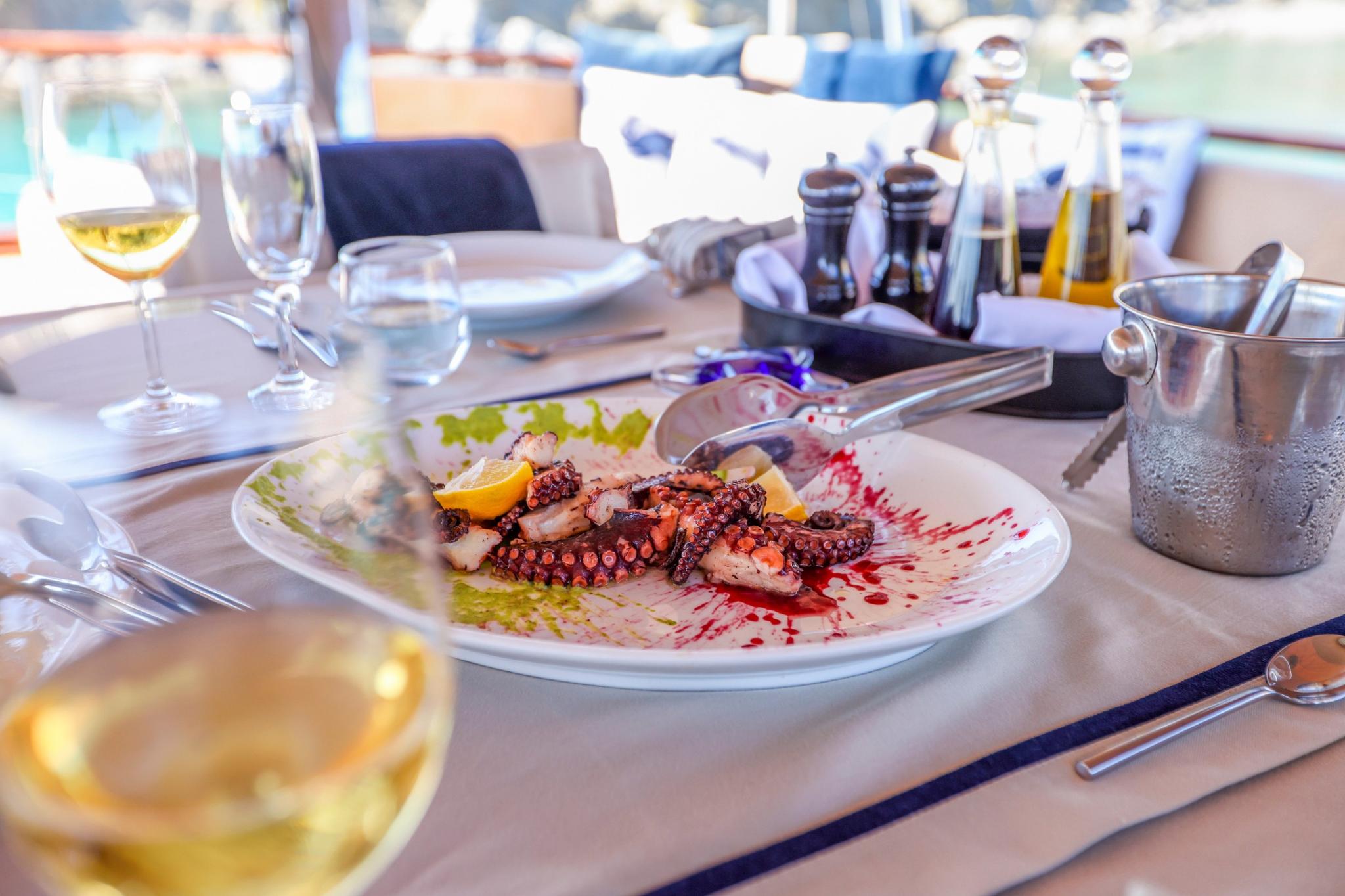 grilled octopus with lemon and sauce served on white plate with wine glasses on yacht dining table
