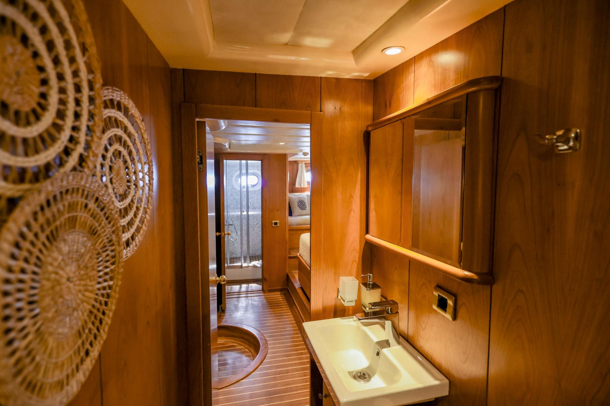 yacht cabin bathroom featuring white sink, mirror, and warm wood paneling throughout