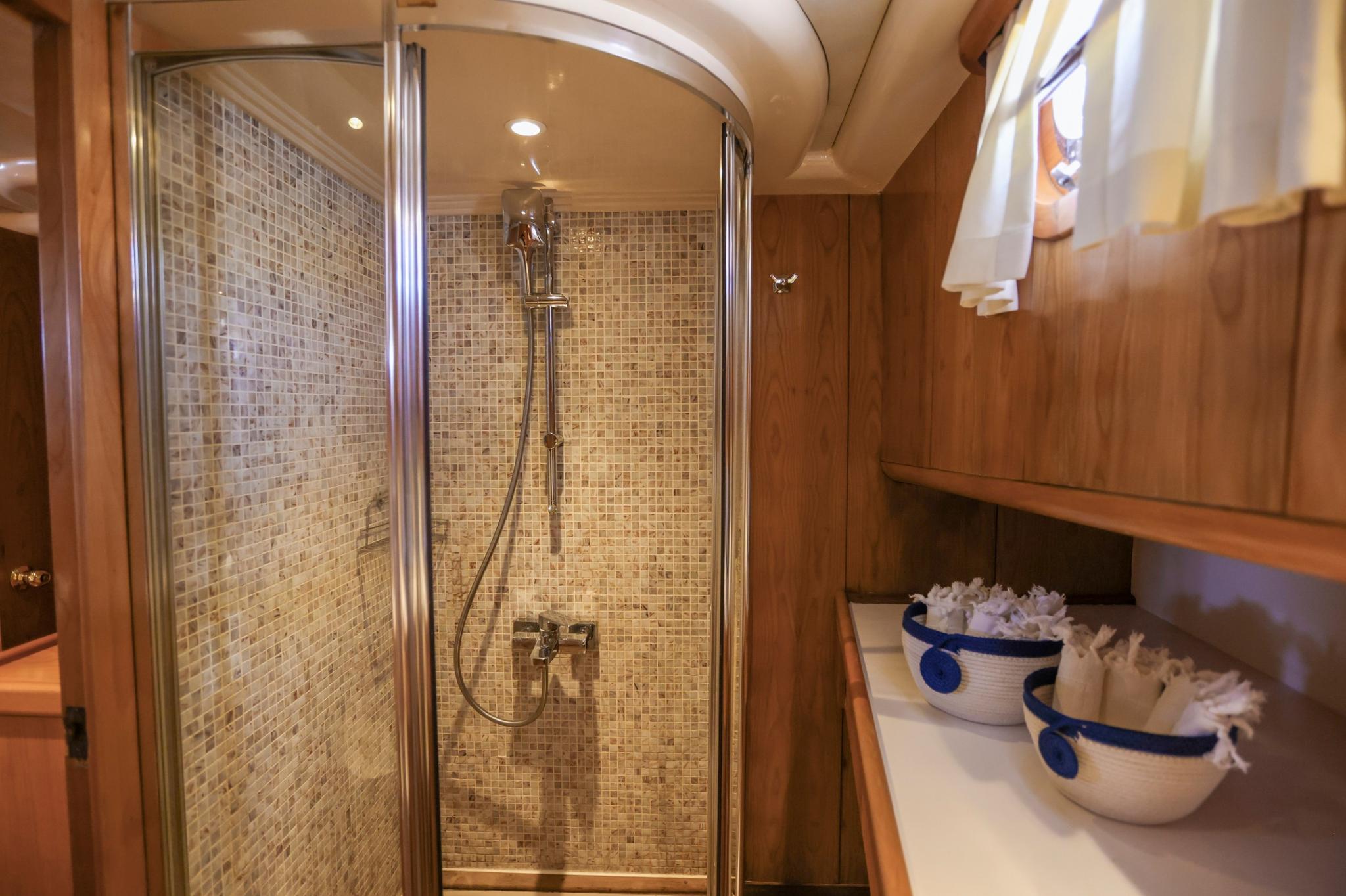 yacht bathroom featuring curved glass shower enclosure with beige mosaic tile walls