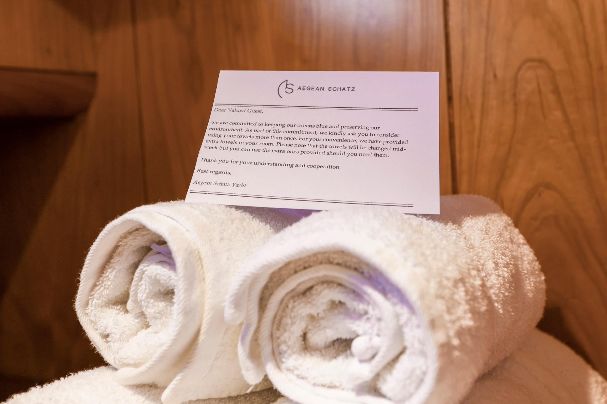rolled white towels with Aegean Schatz yacht welcome note in cabin