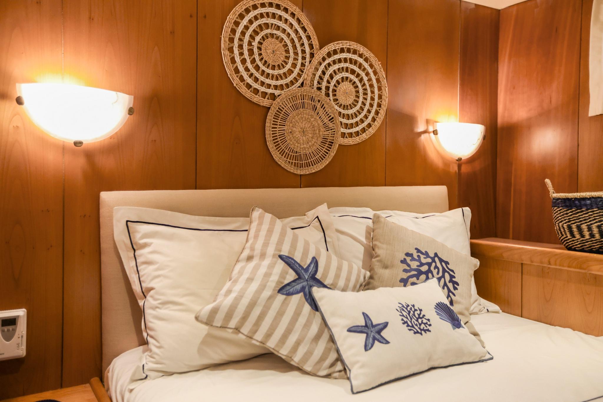 yacht guest cabin featuring double bed with blue nautical cushions and woven basket wall art