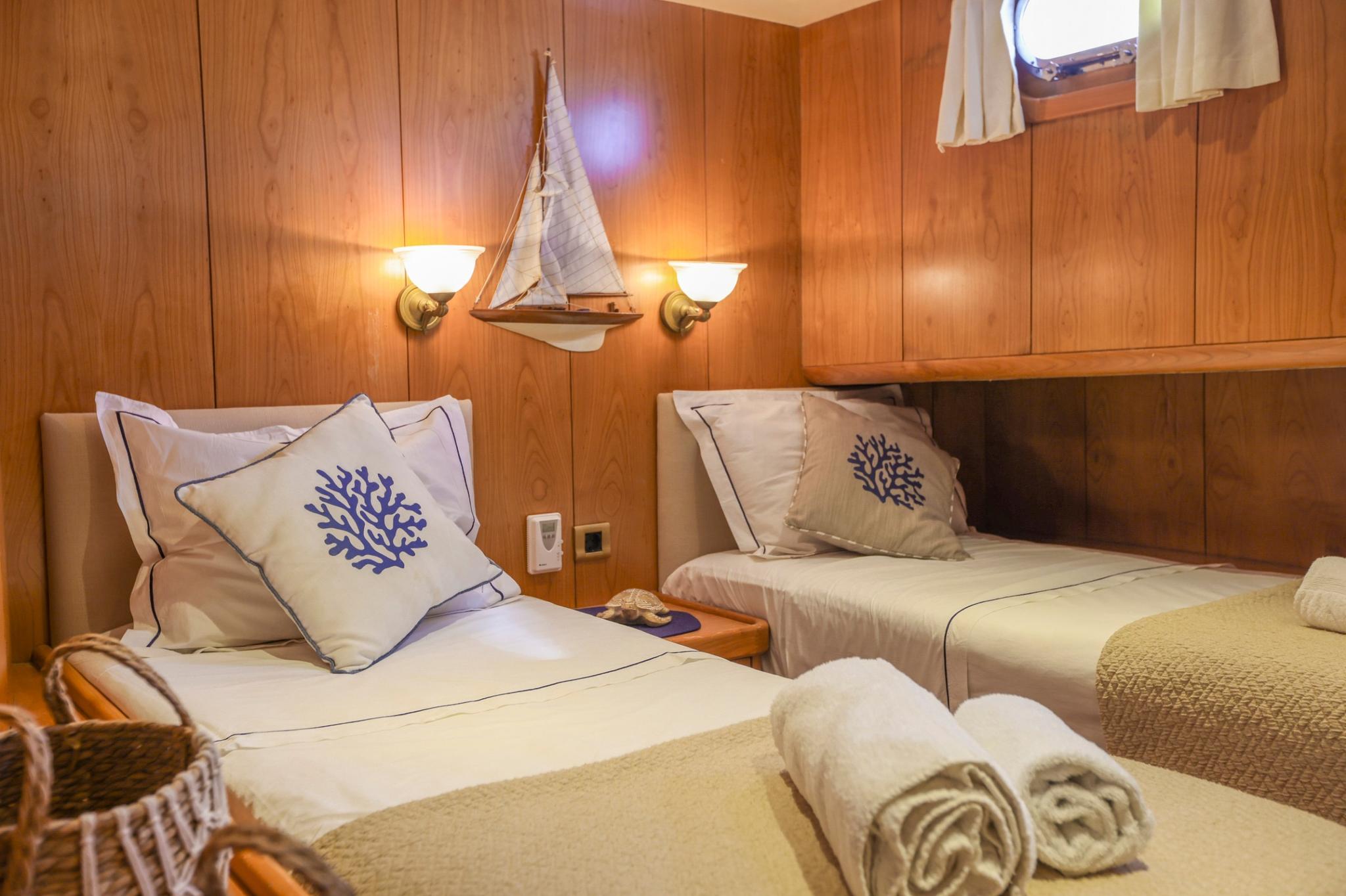 yacht guest cabin featuring twin beds with blue coral embroidered pillows and warm wood paneling