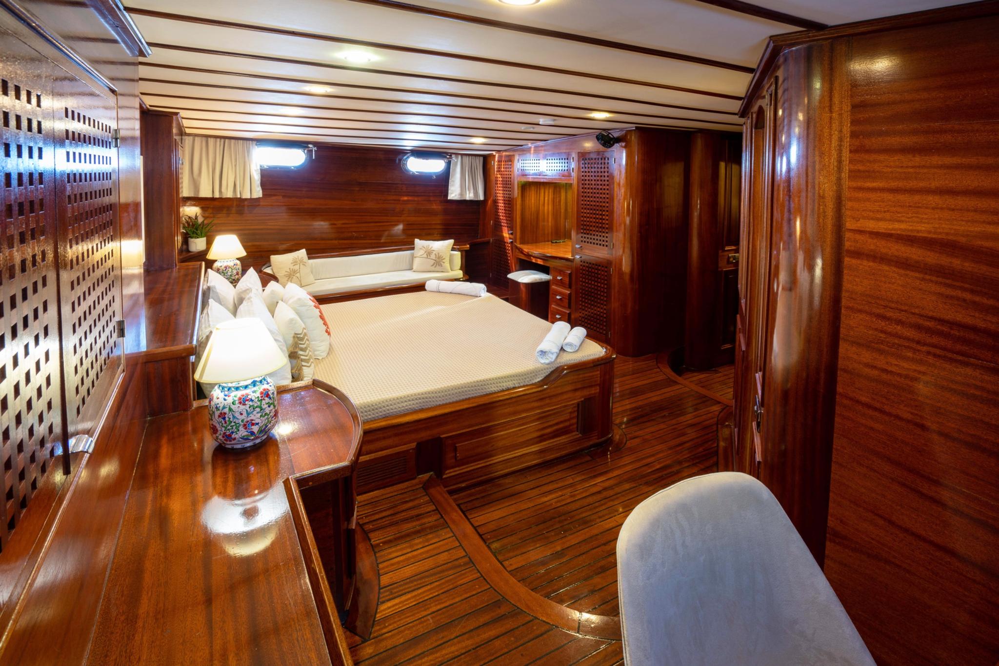 elegant yacht guest cabin featuring double bed with white linens and curved seating bench