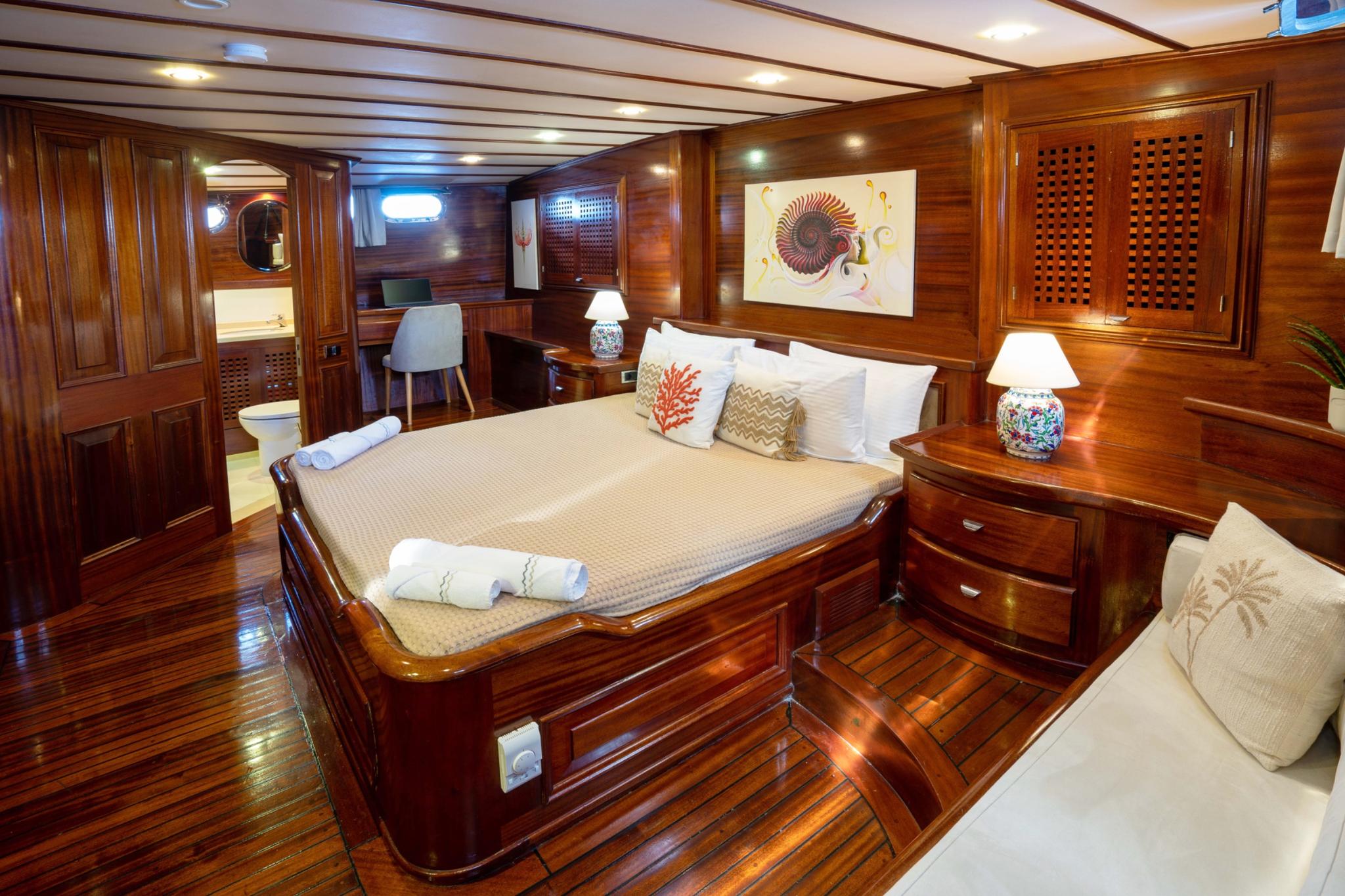 Master cabin featuring double bed, rich mahogany wood paneling, built-in nightstands with decorative lamps