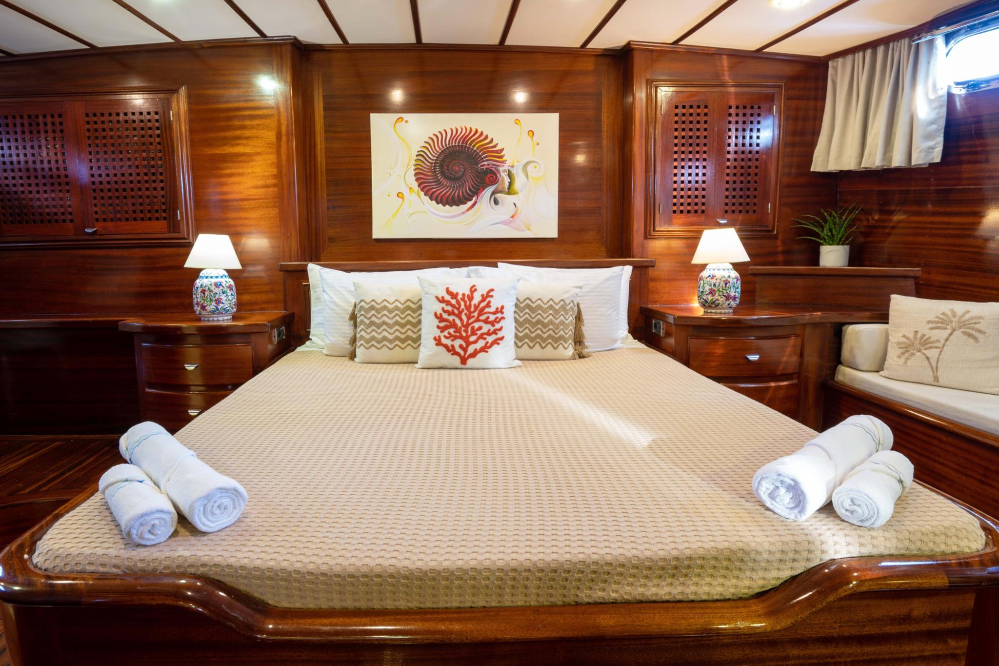 yacht cabin interior with double bed, rich wood paneling, decorative artwork and built-in nightstands
