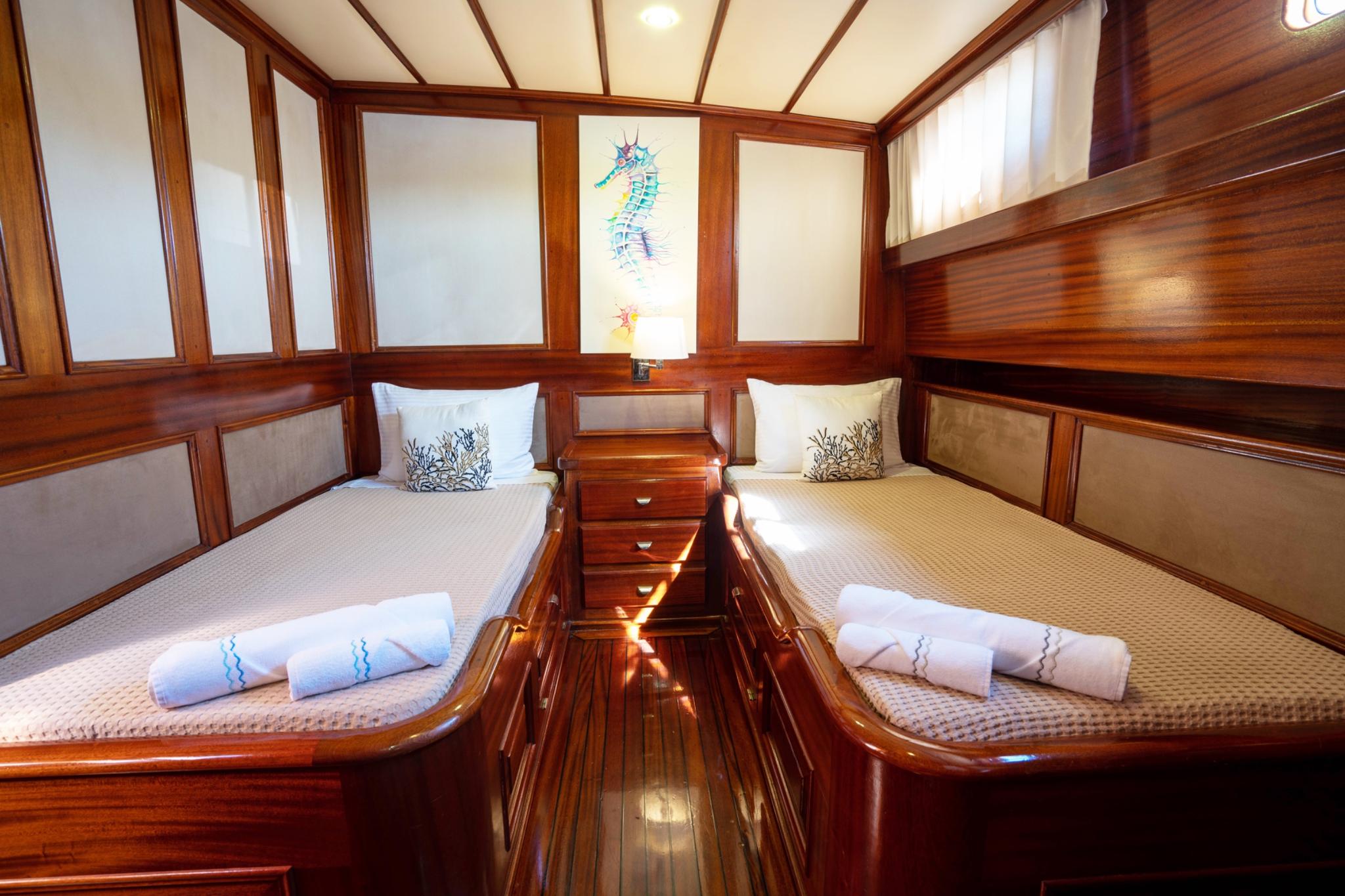 yacht twin cabin with two single beds, wooden nightstand and seahorse artwork