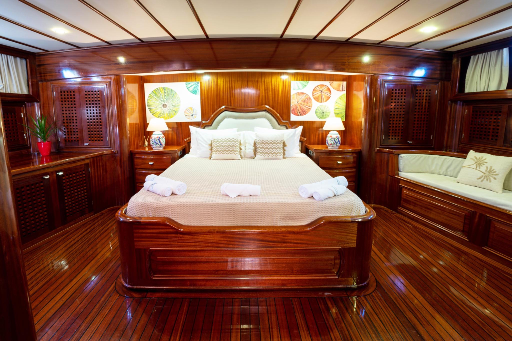 Master cabin interior with king bed, rich mahogany woodwork, built-in wardrobes and seating area