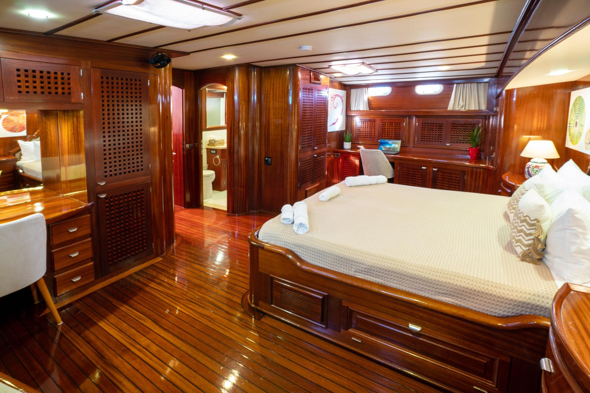 Luxury yacht master cabin with king bed, rich mahogany woodwork and en-suite bathroom entrance