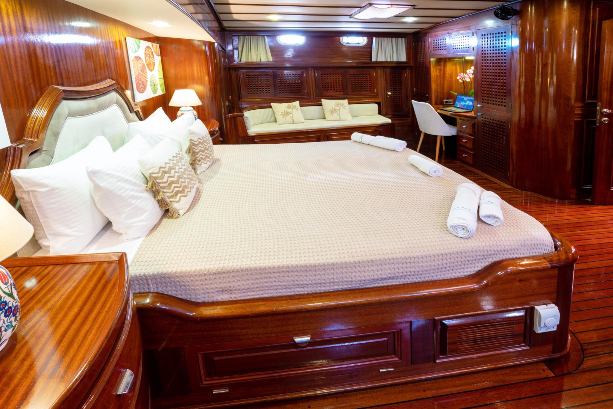 Luxury yacht master cabin featuring king bed with white linens, built-in seating area, and polished wood paneling