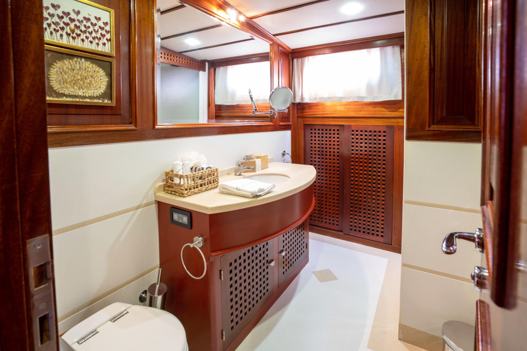 luxury yacht bathroom featuring curved marble vanity, integrated sink, porthole windows and wooden cabinetry