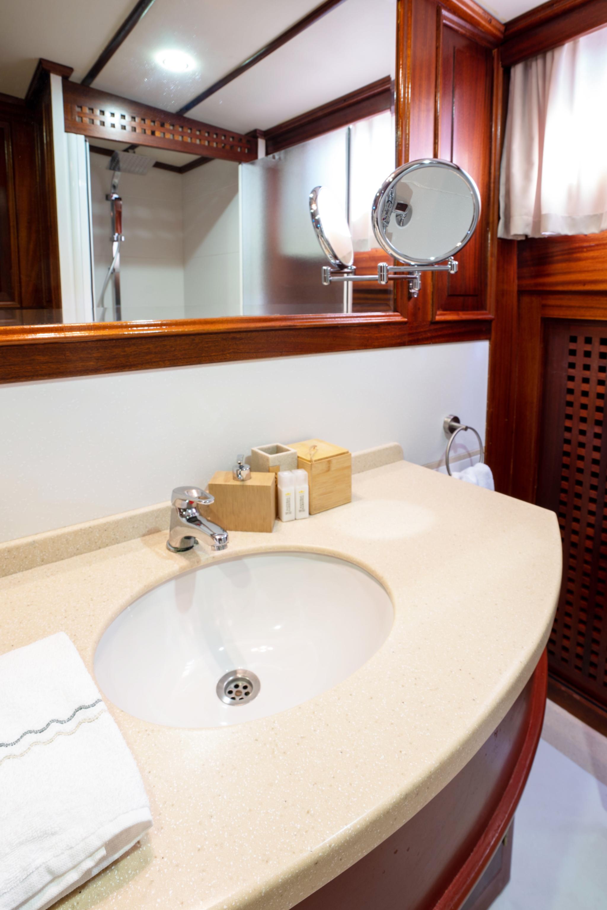 yacht bathroom featuring curved beige stone vanity, round basin, chrome fixtures and wood paneling