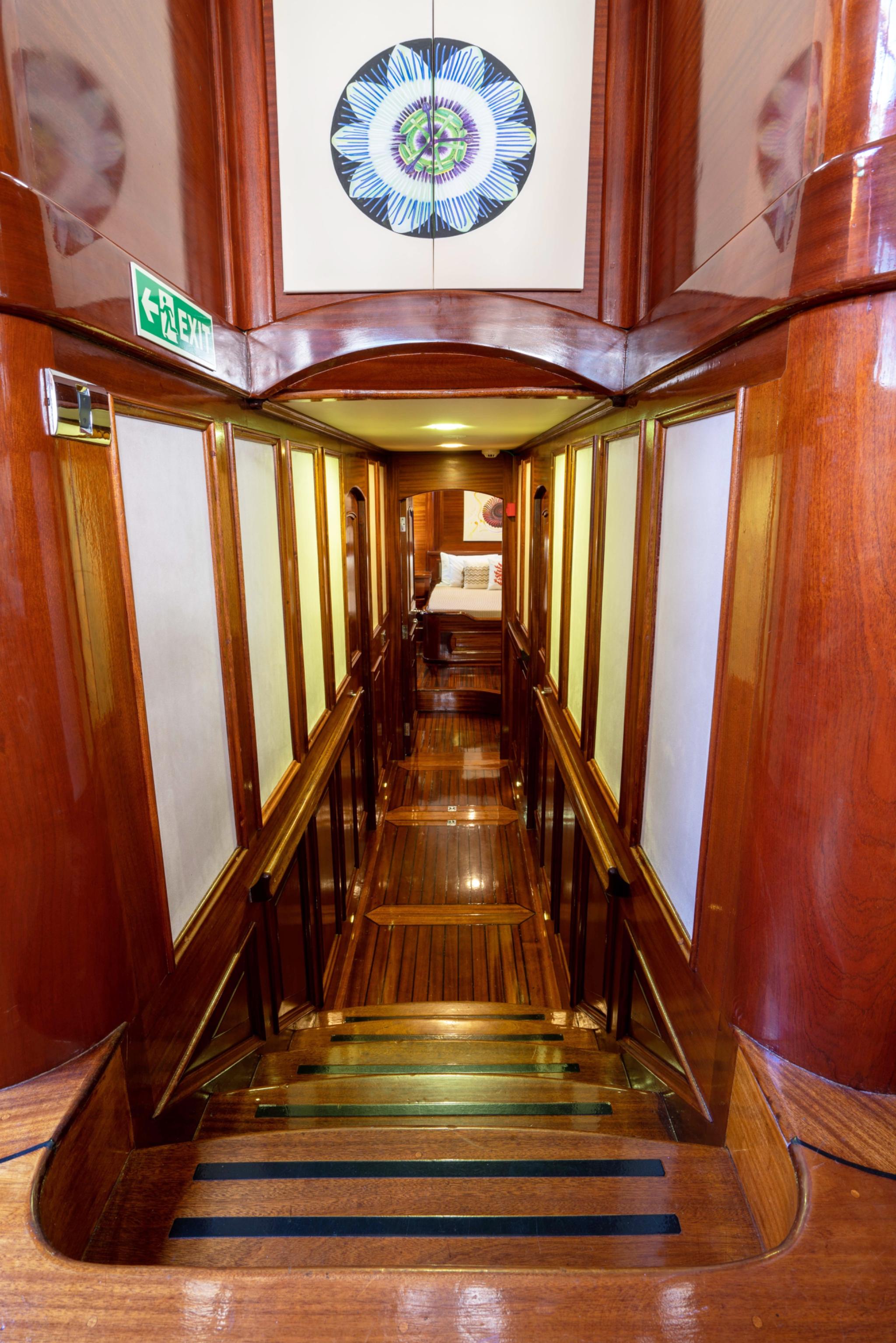 yacht interior corridor with polished wood paneling, stairs leading down, and circular decorative skylight overhead