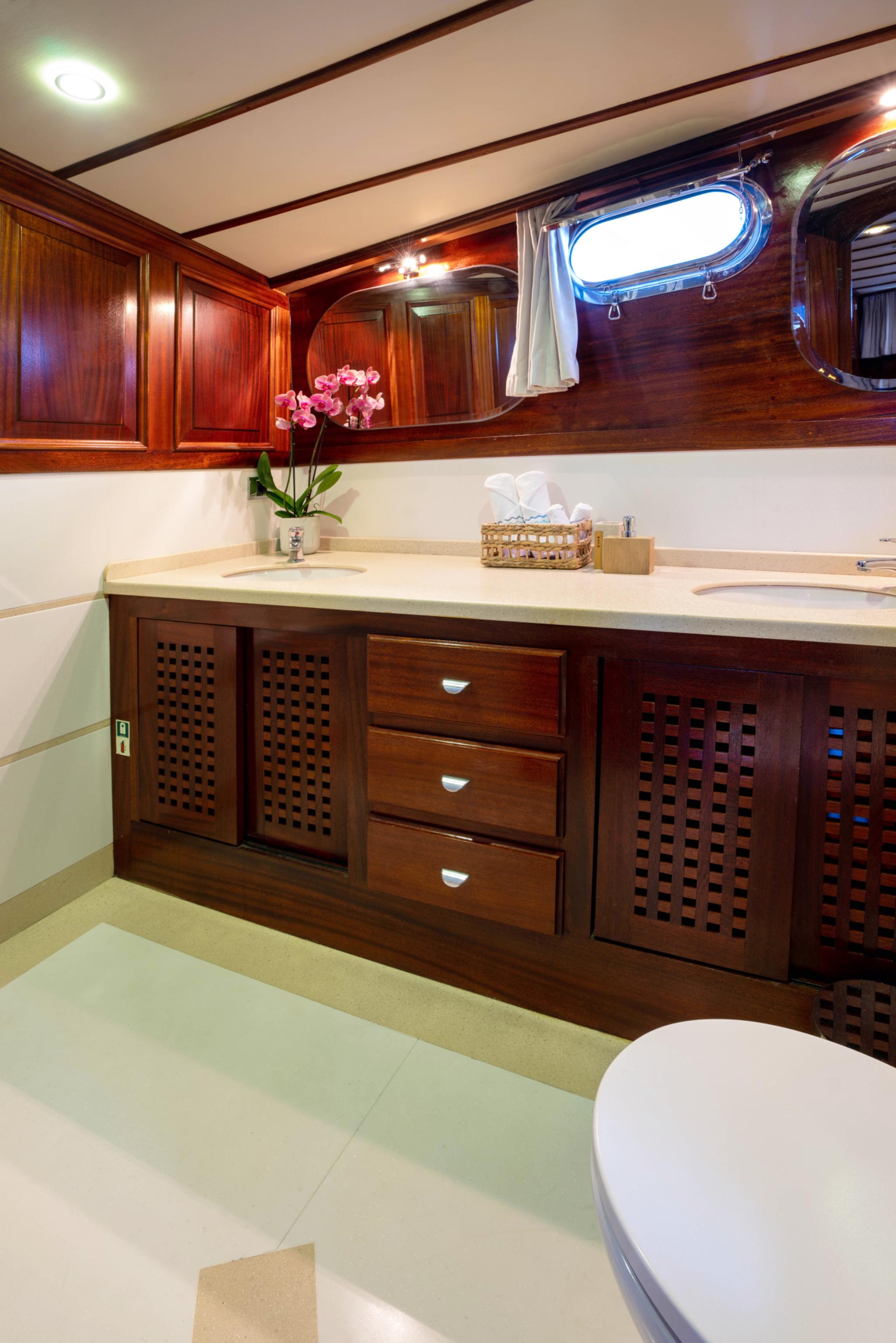 yacht bathroom featuring dual sinks, marble countertop, wooden cabinetry with ventilation panels