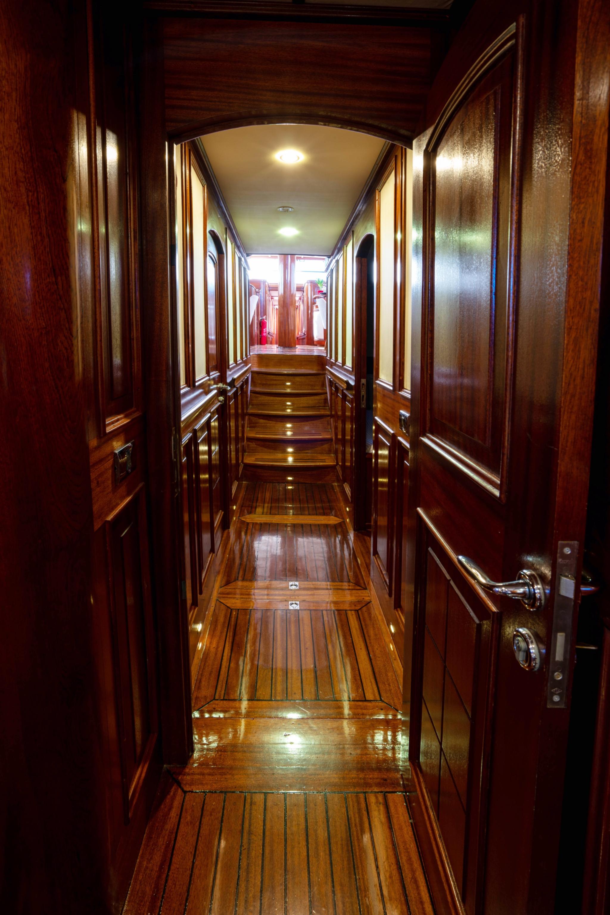 wooden interior corridor with stairs leading down, polished mahogany paneling and handrails