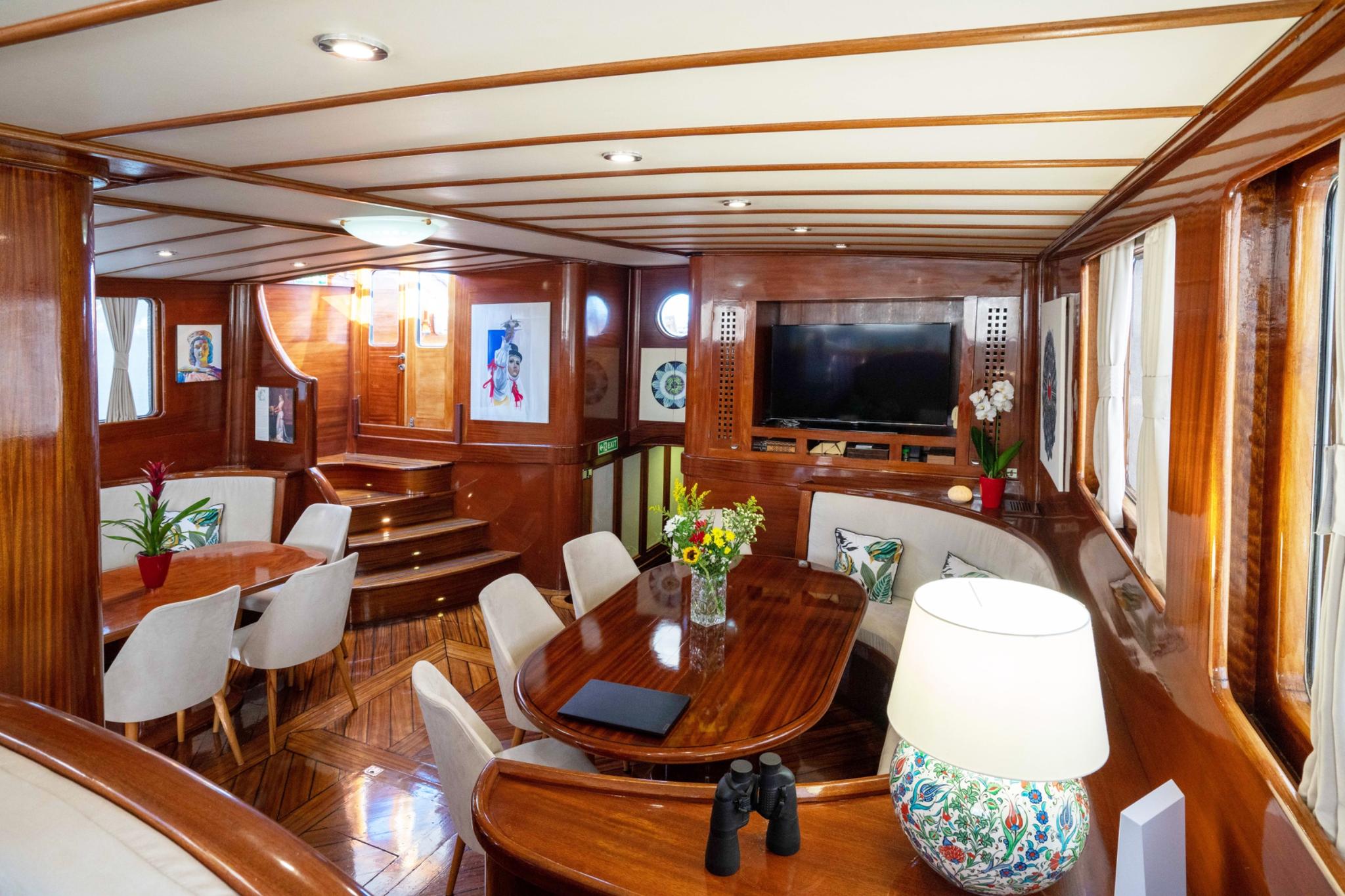 luxury yacht main salon with oval dining table, white chairs, and built-in TV entertainment unit