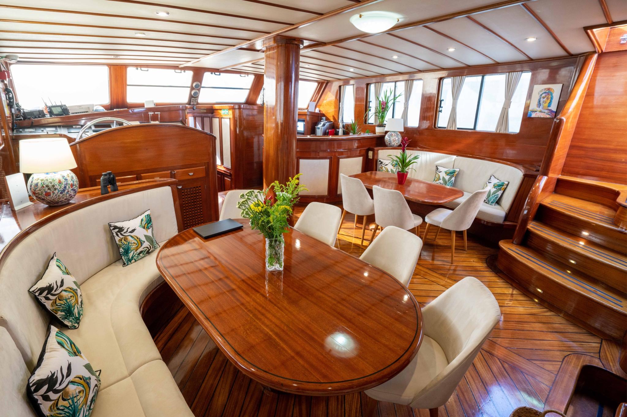 yacht main salon interior with oval dining table, cream chairs and built-in banquette seating