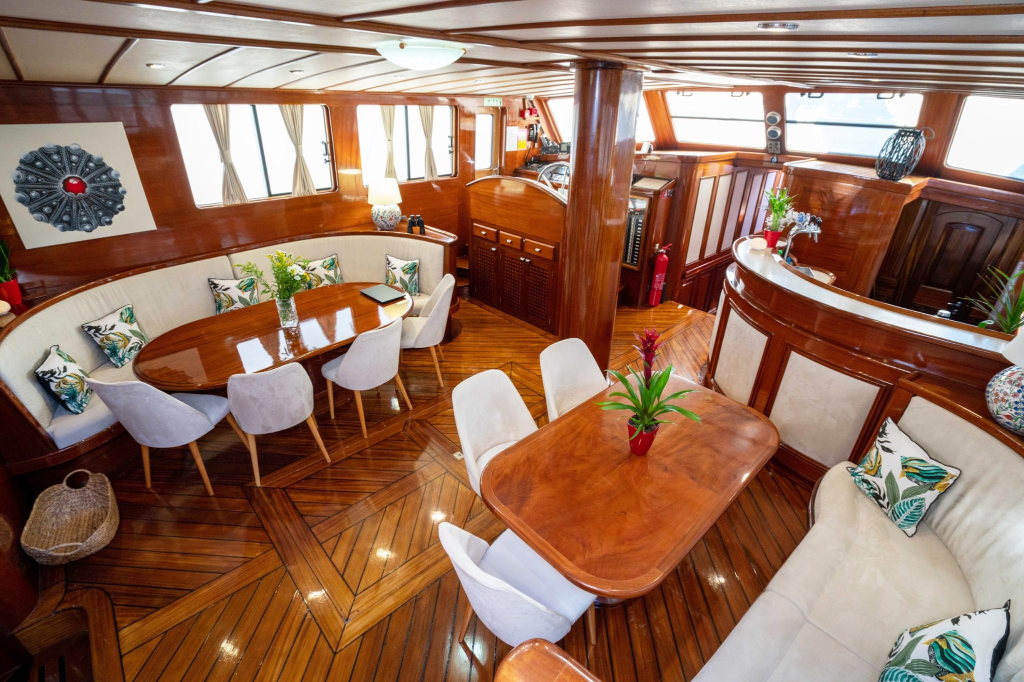 yacht salon interior with curved banquette seating, dining tables, and tropical leaf cushions