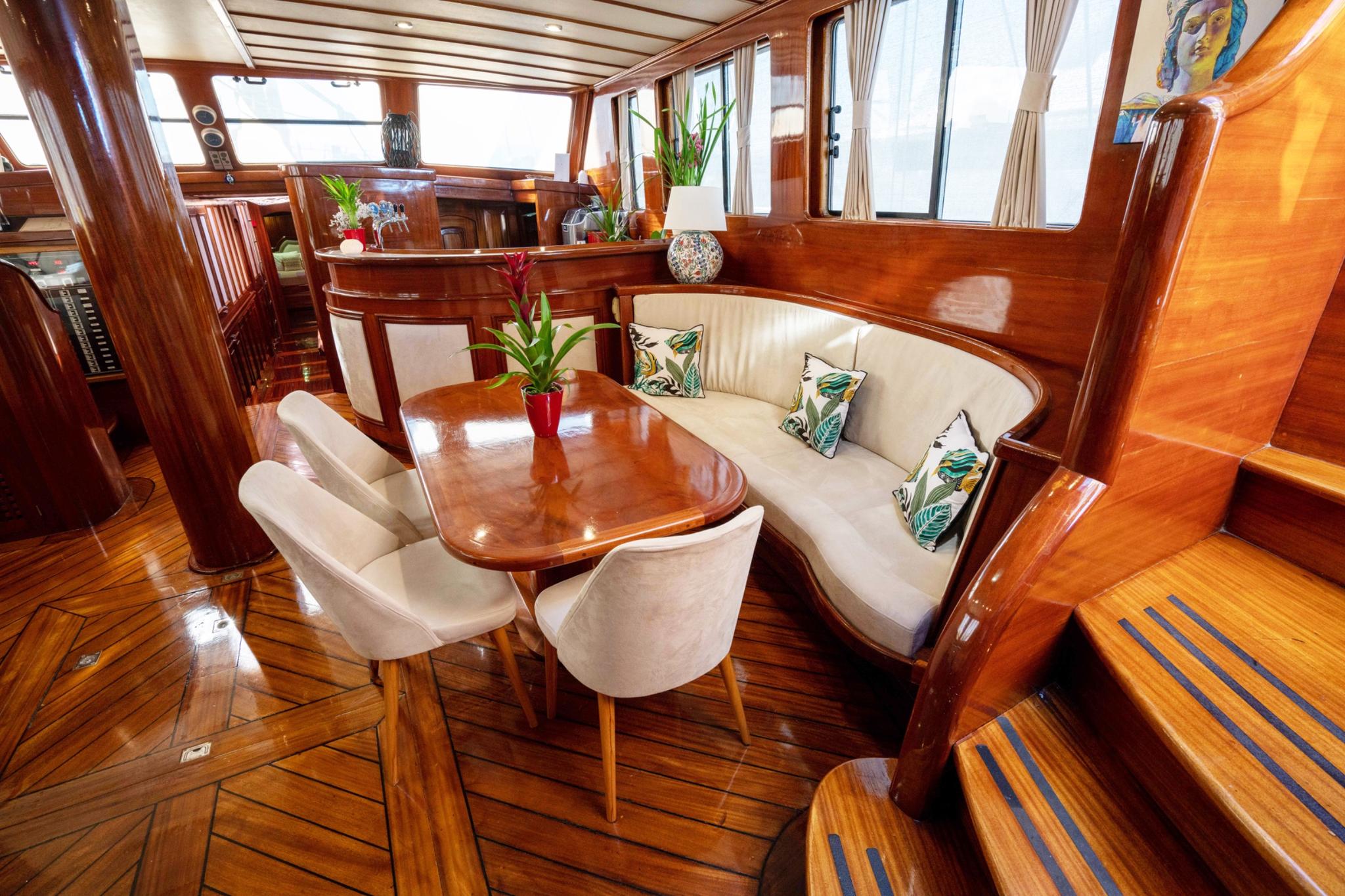 yacht interior salon with curved cream banquette seating, polished wood dining table, and tropical cushions