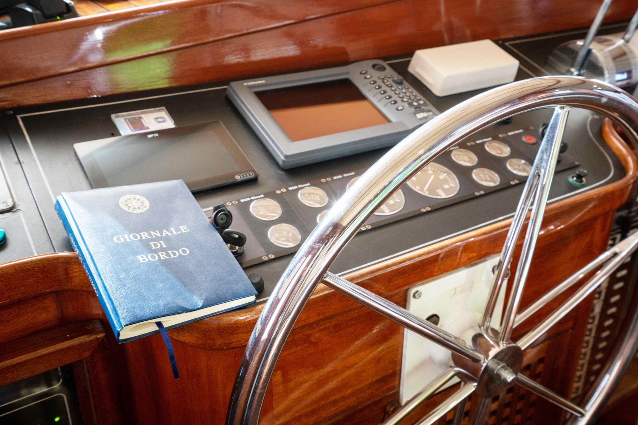 yacht helm station with polished steering wheel, instrument panel, chart plotter and ship's log book