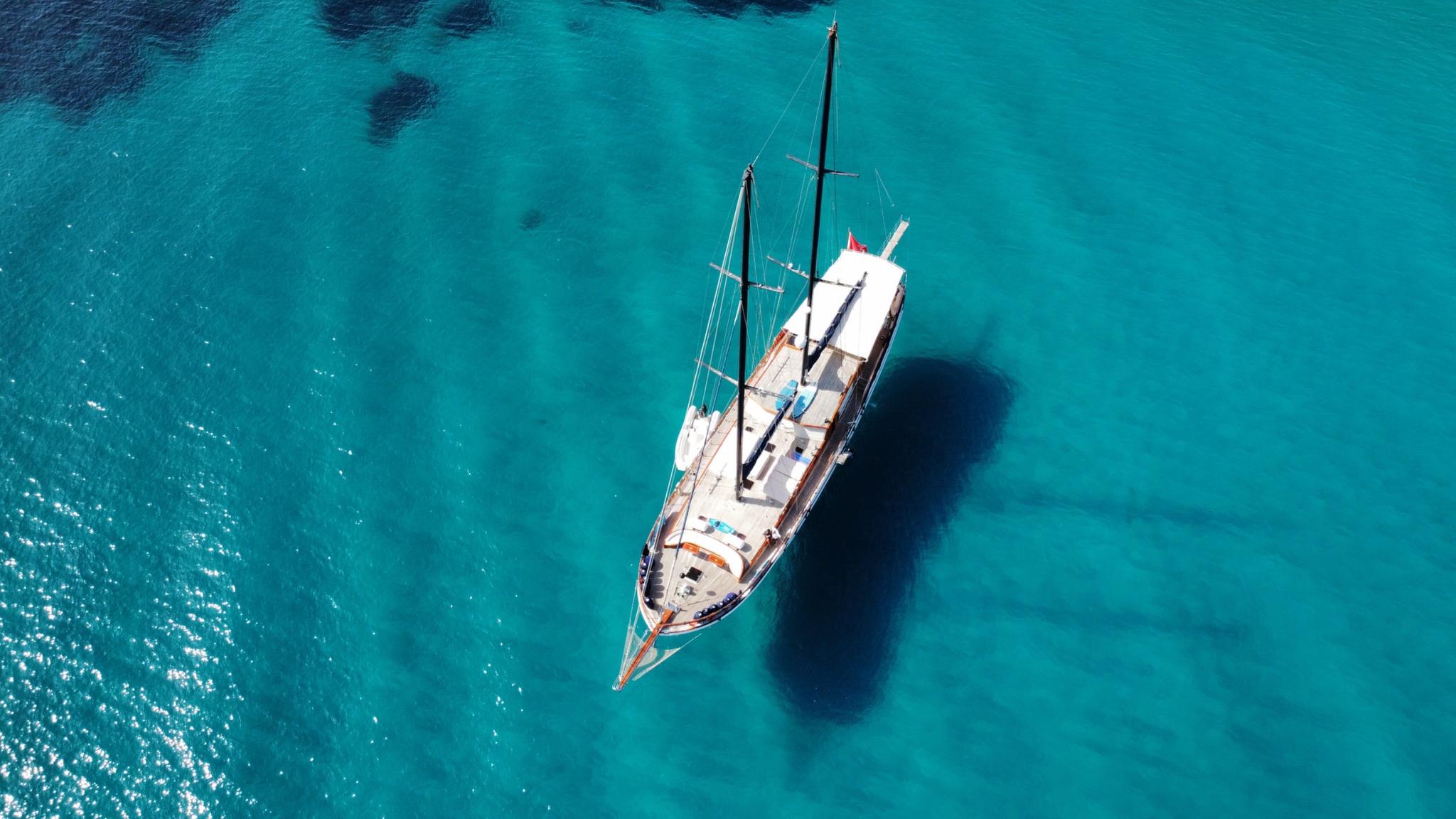 aerial view of traditional gulet yacht with two masts anchored in crystal clear turquoise bay