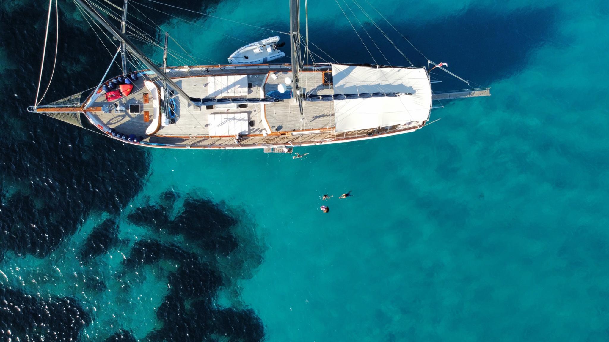 aerial view of white sailing yacht at anchor in crystal clear turquoise waters with swimmers nearby