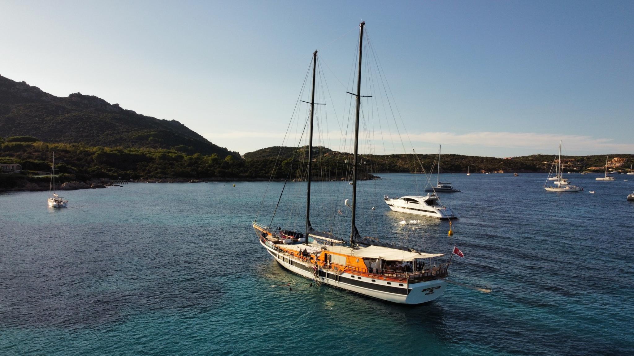 wooden gulet yacht anchored in turquoise bay surrounded by hills and other boats