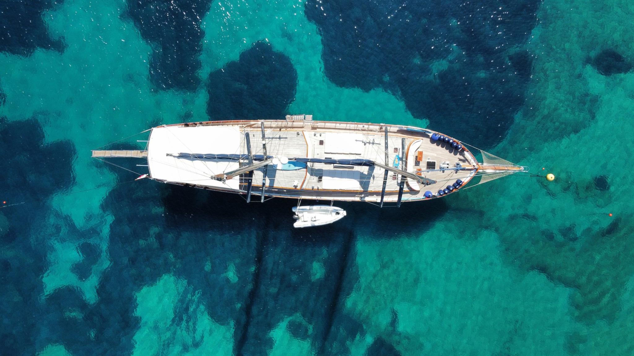 aerial view of white gulet yacht with tender boat anchored in crystal clear turquoise waters