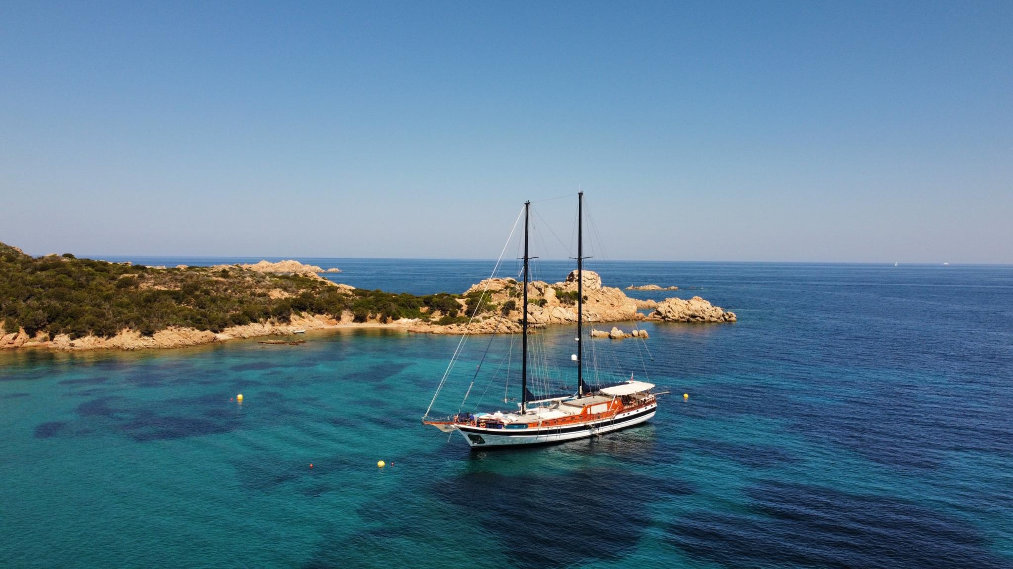 aerial view of traditional gulet yacht anchored in crystal clear turquoise waters near Mediterranean rocky coastline