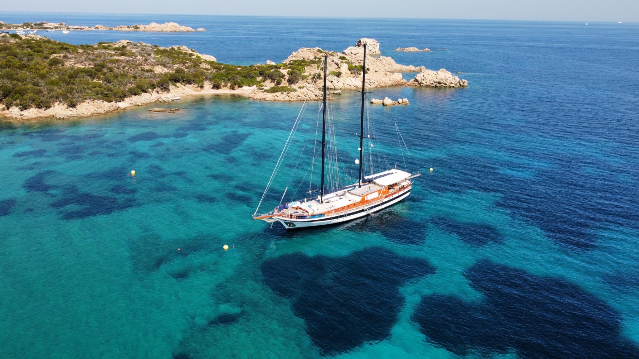 aerial view of traditional gulet yacht anchored in crystal clear turquoise waters near rocky coastline