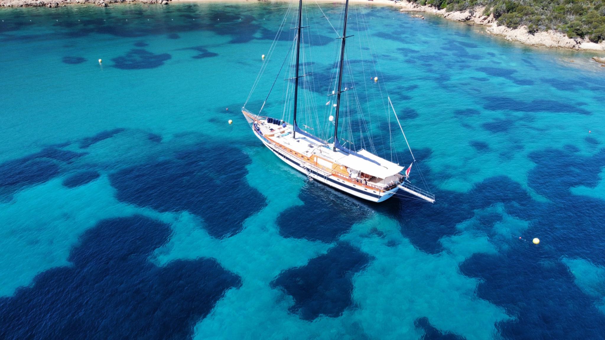 aerial view of white gulet with two masts anchored in crystal clear turquoise waters