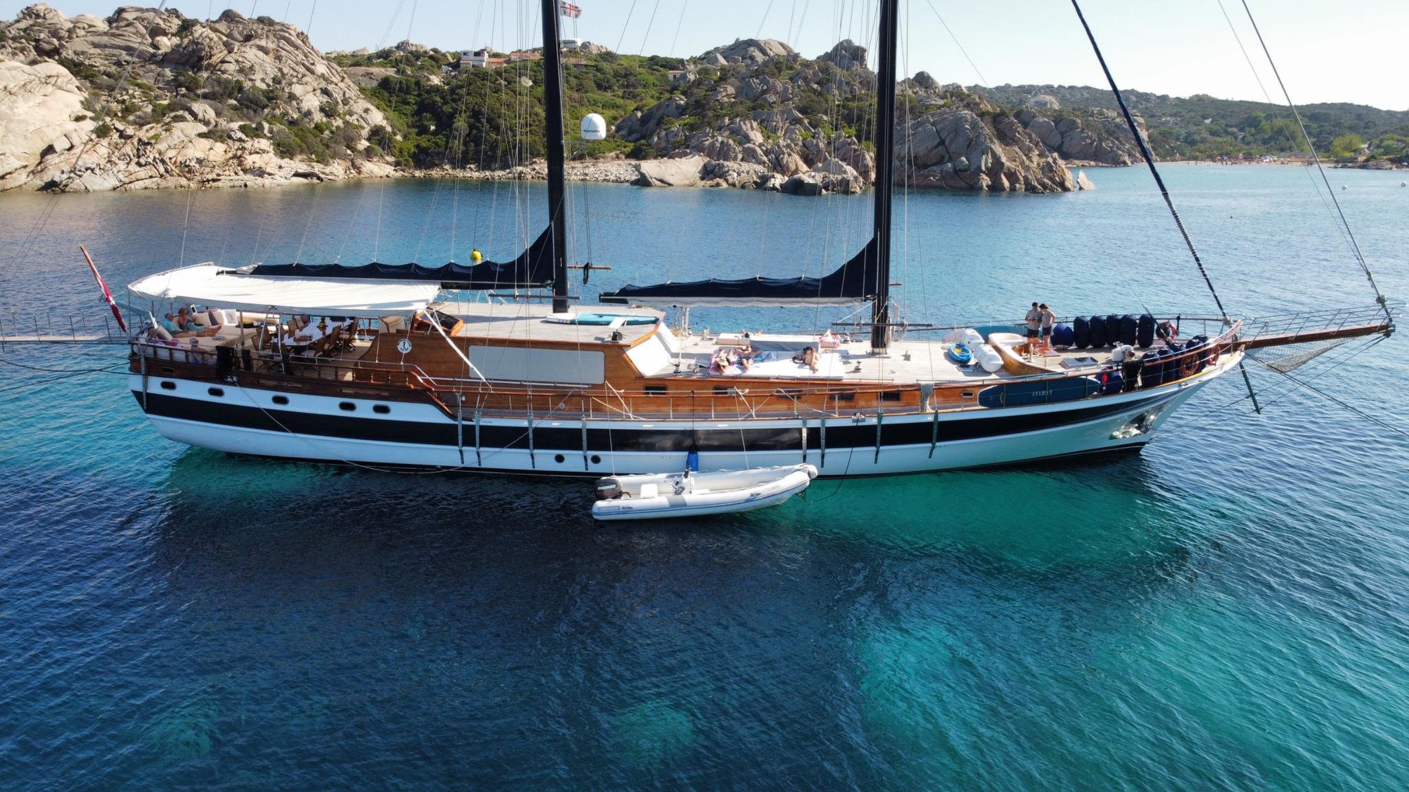 Traditional wooden gulet with white hull and teak decks anchored in crystal clear turquoise waters