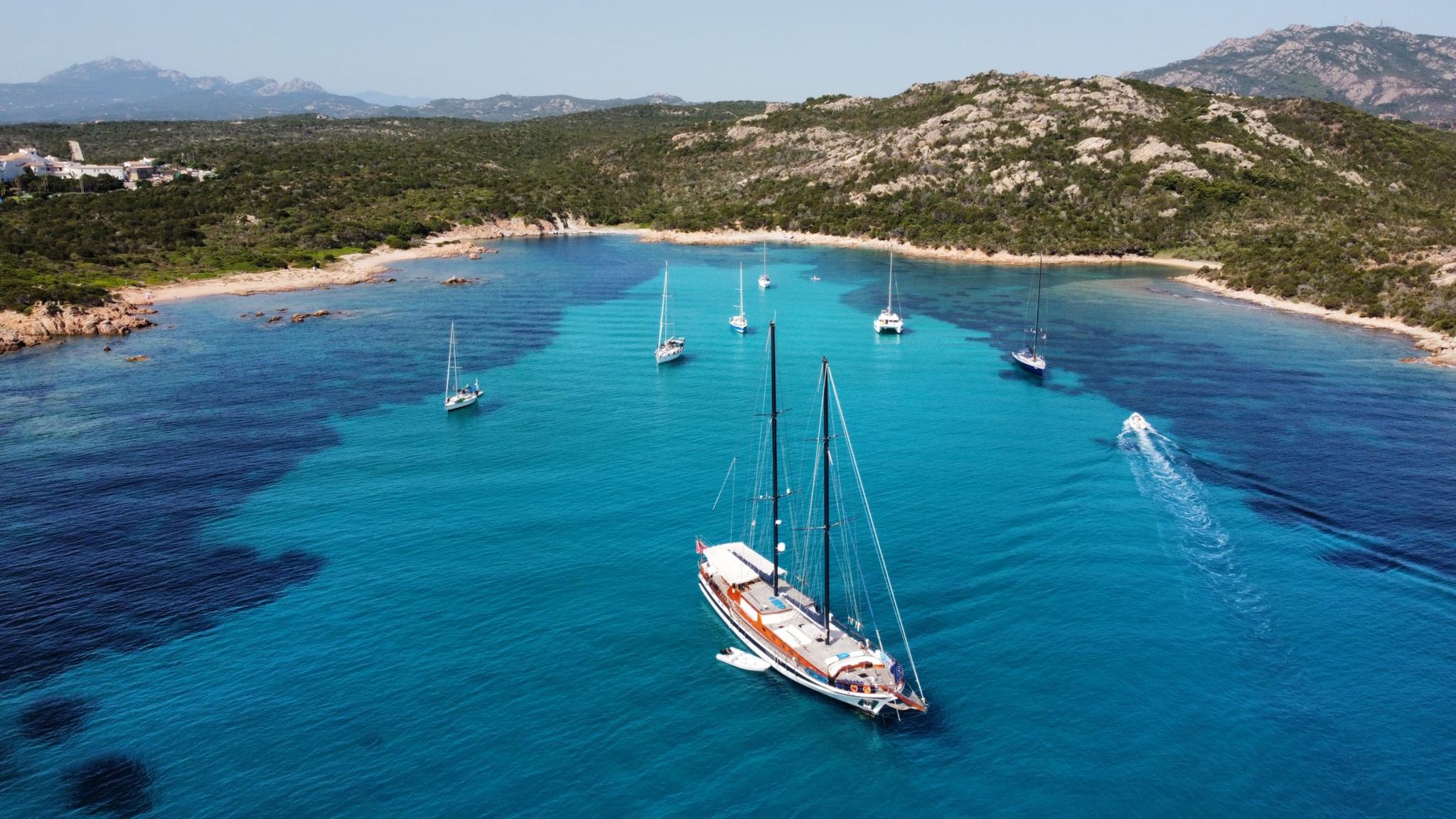 aerial view of traditional gulet anchored in crystal clear turquoise bay surrounded by rocky coastline