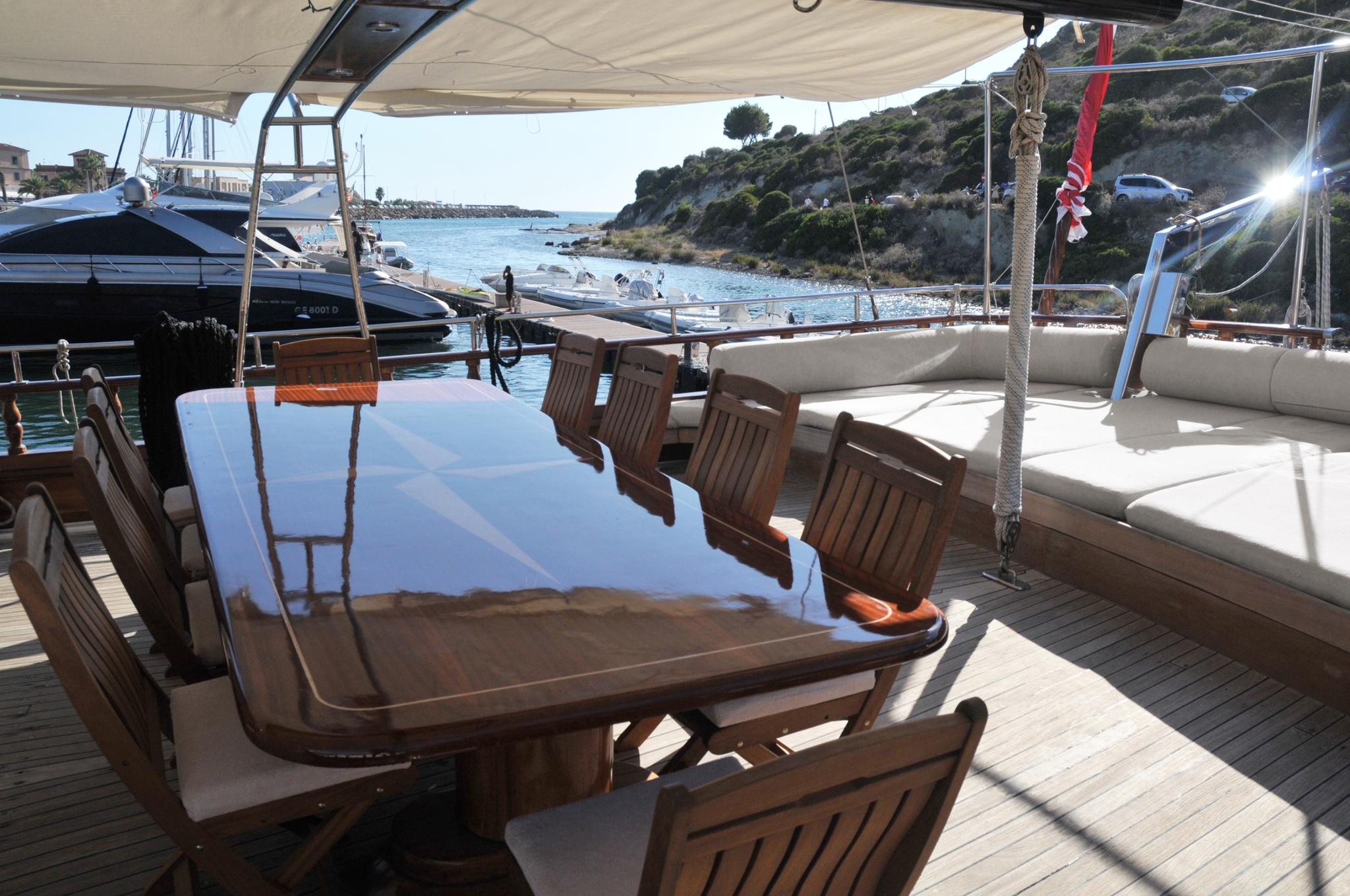 yacht aft deck with teak dining table, wooden chairs and white cushioned seating area