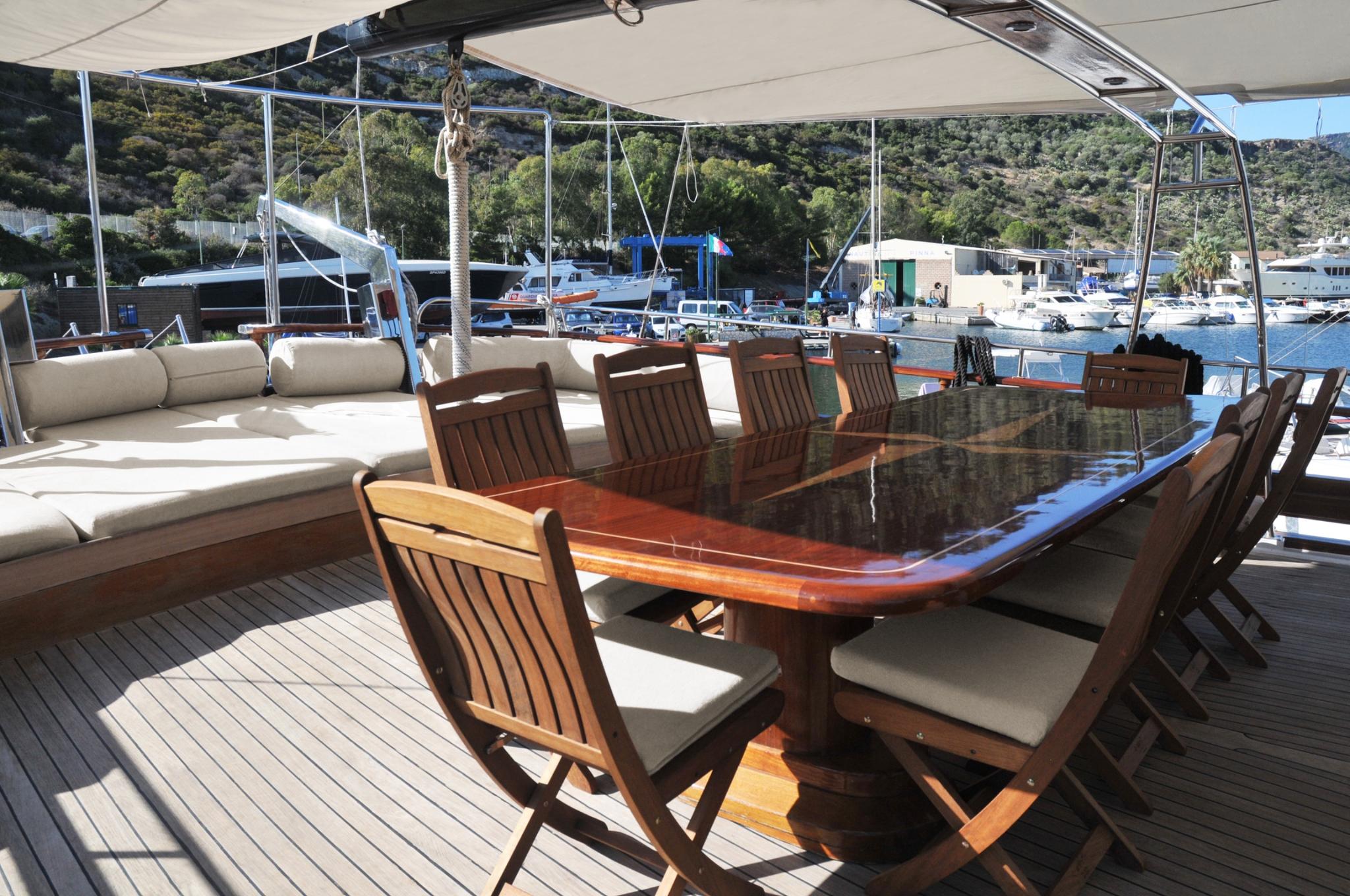 aft deck outdoor dining area with large wooden table, teak chairs and L-shaped seating