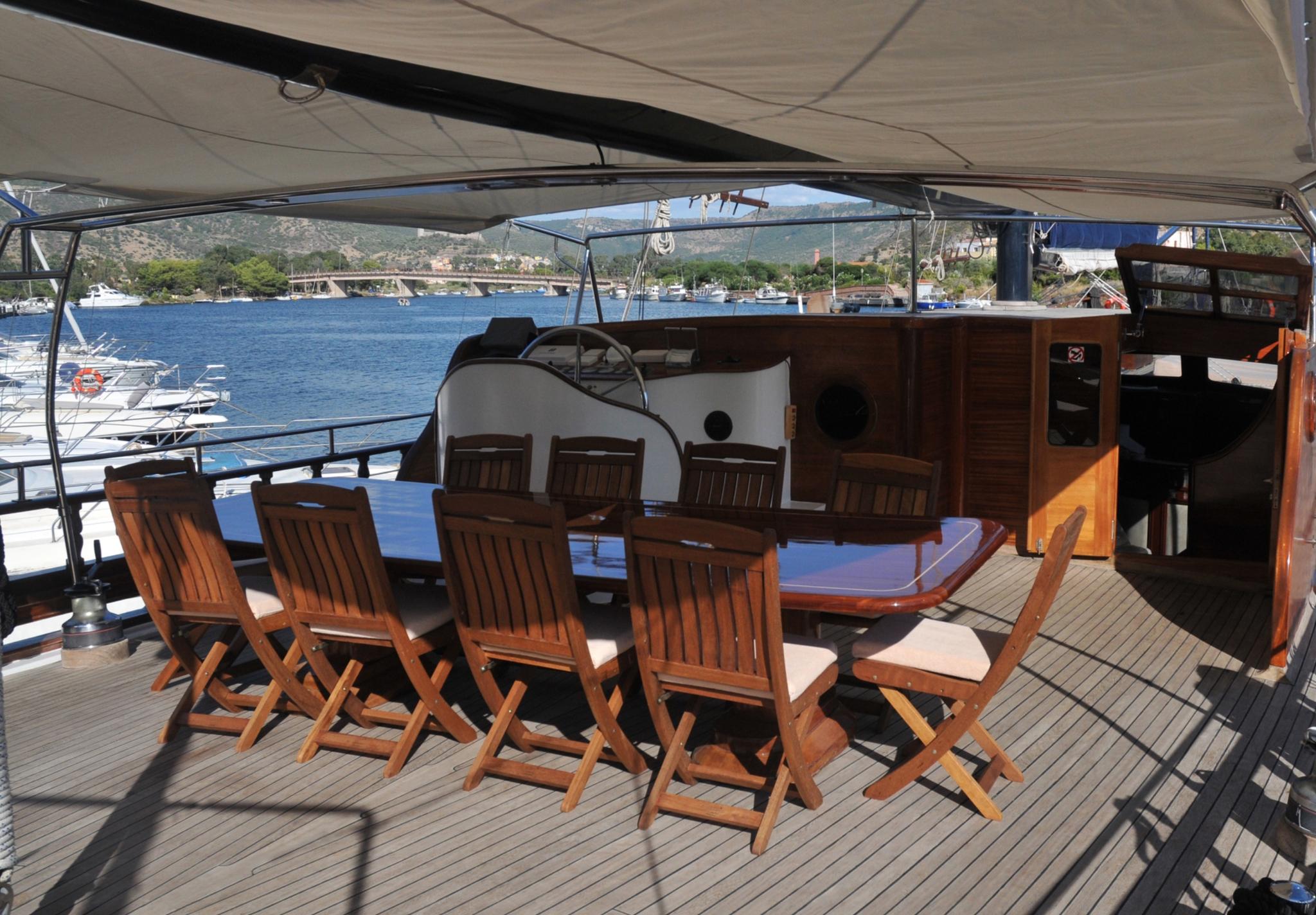 gulet aft deck outdoor dining area with wooden table and folding chairs under awning