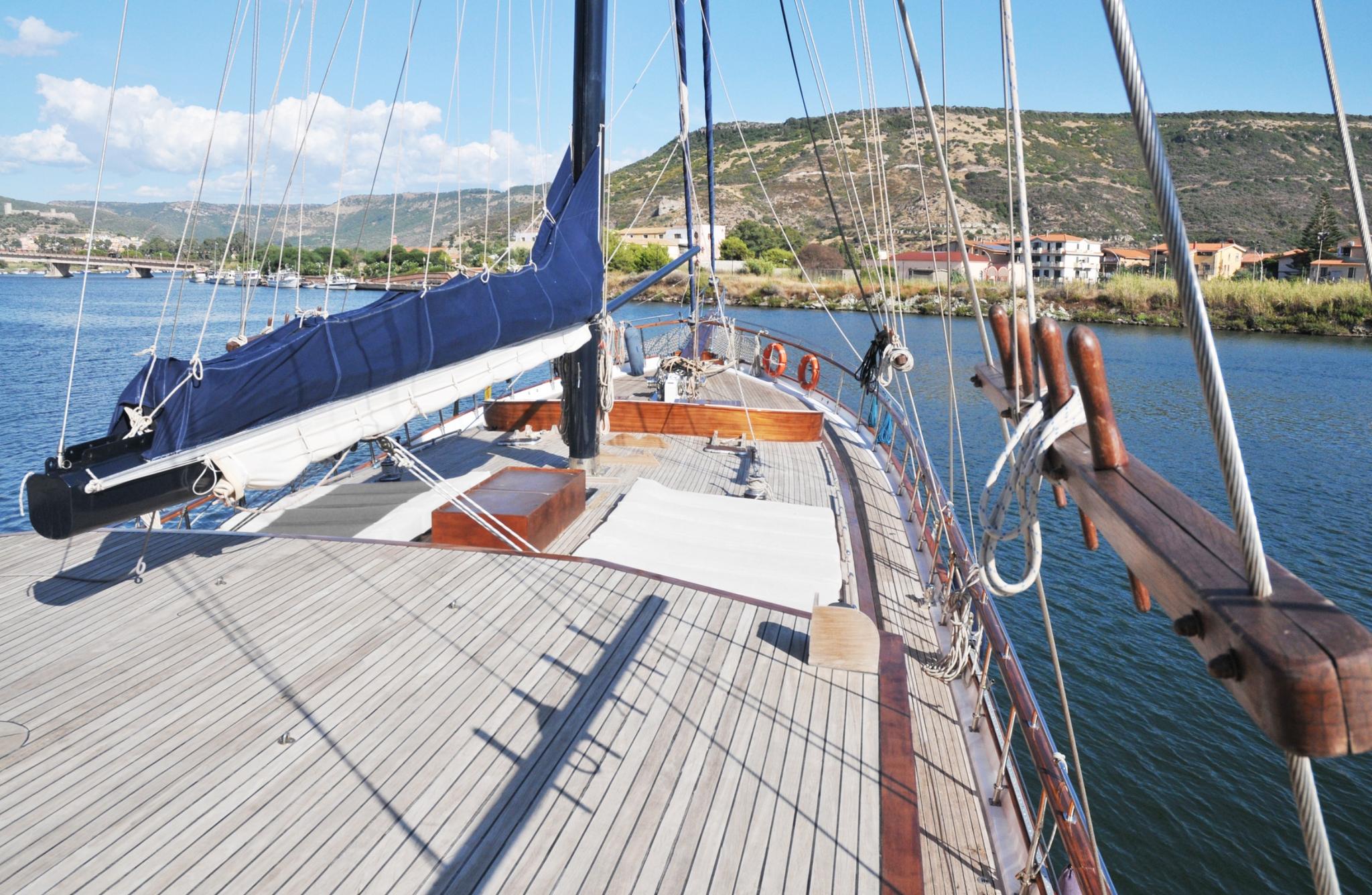 gulet forward deck with teak planking, furled blue sail, and rigging anchored in bay