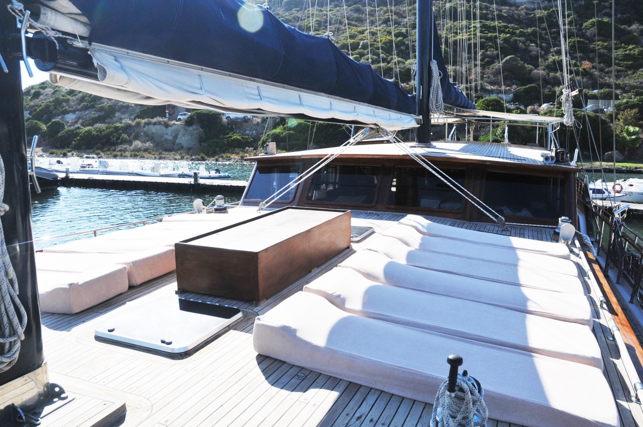 bow sun deck with white cushioned loungers and wooden storage console on luxury gulet