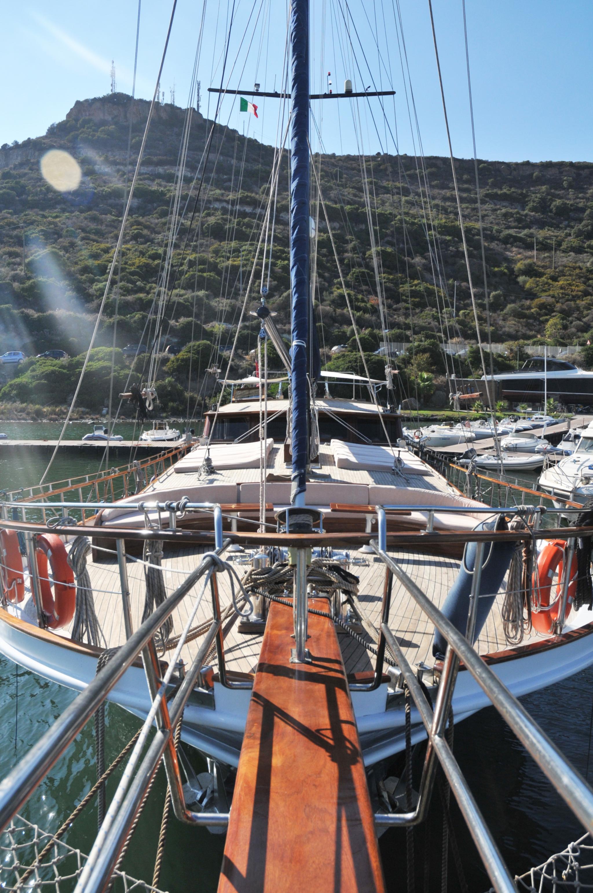 Gulet aft deck showing wooden dining table, helm station, rigging and mast from stern perspective