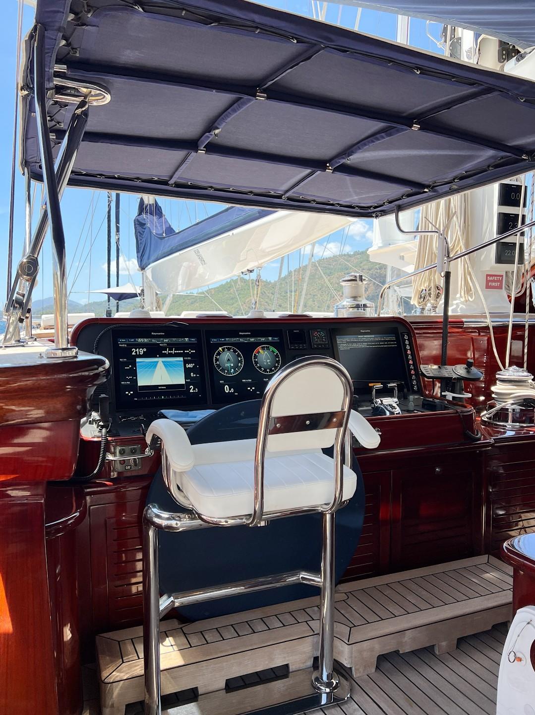 yacht helm station showing digital navigation displays, gauges, and white captain's chair with mahogany woodwork