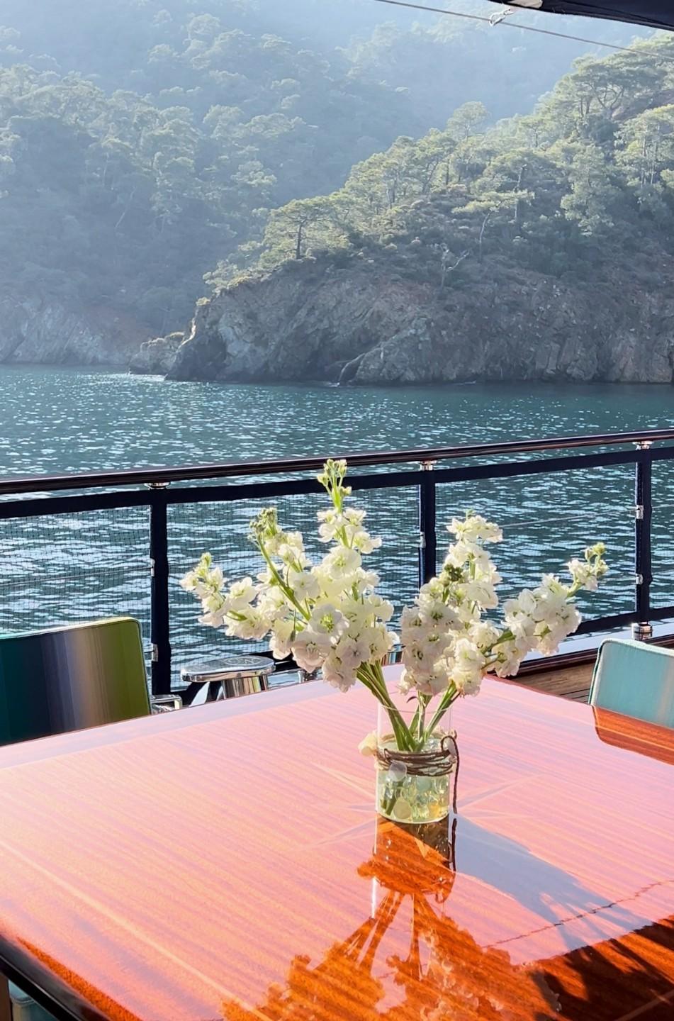 yacht aft deck dining area with white flowers in glass vase overlooking rocky coastline