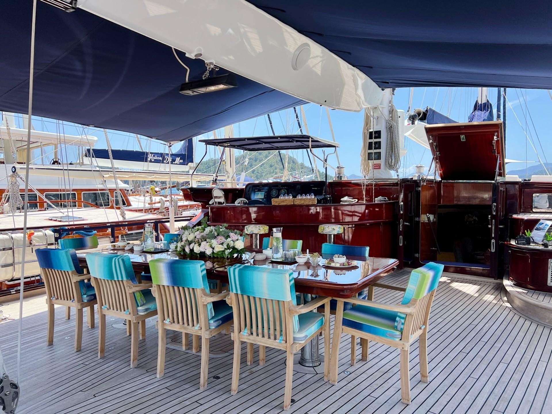 Aft deck dining area with wooden table, blue striped chairs and marina view