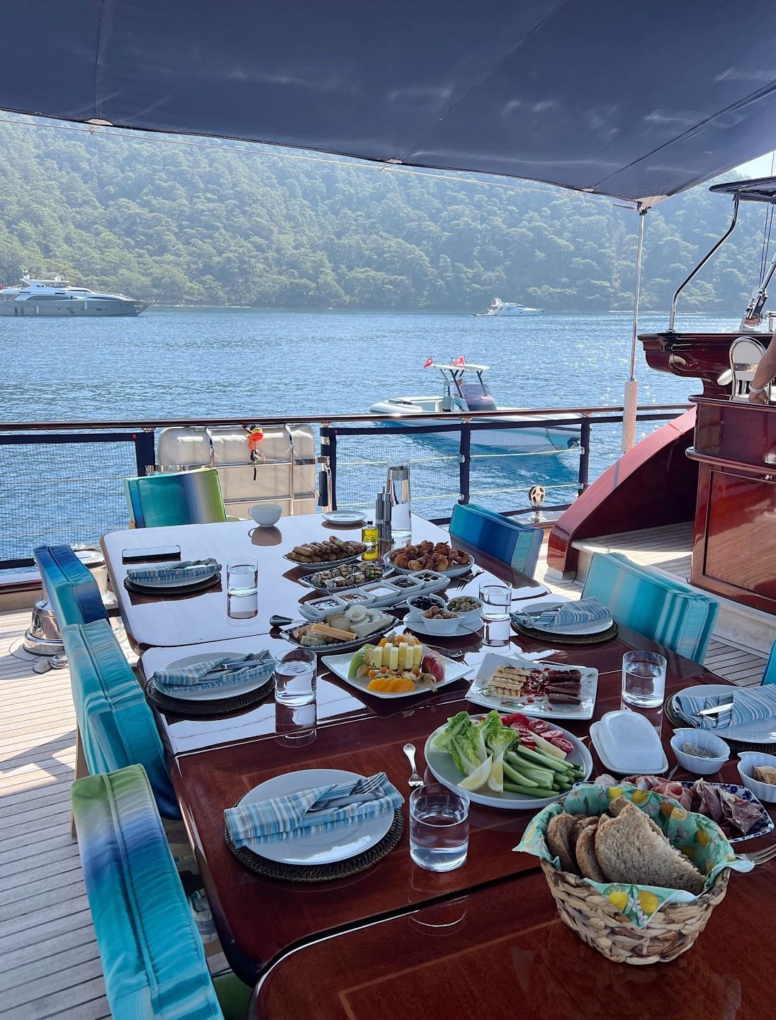 Aft deck dining table set with Turkish breakfast spread including cheese, olives, bread and fresh vegetables