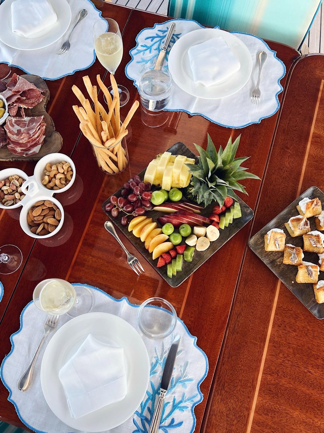luxury yacht dining table with fruit platter, charcuterie, breadsticks, nuts and formal place settings
