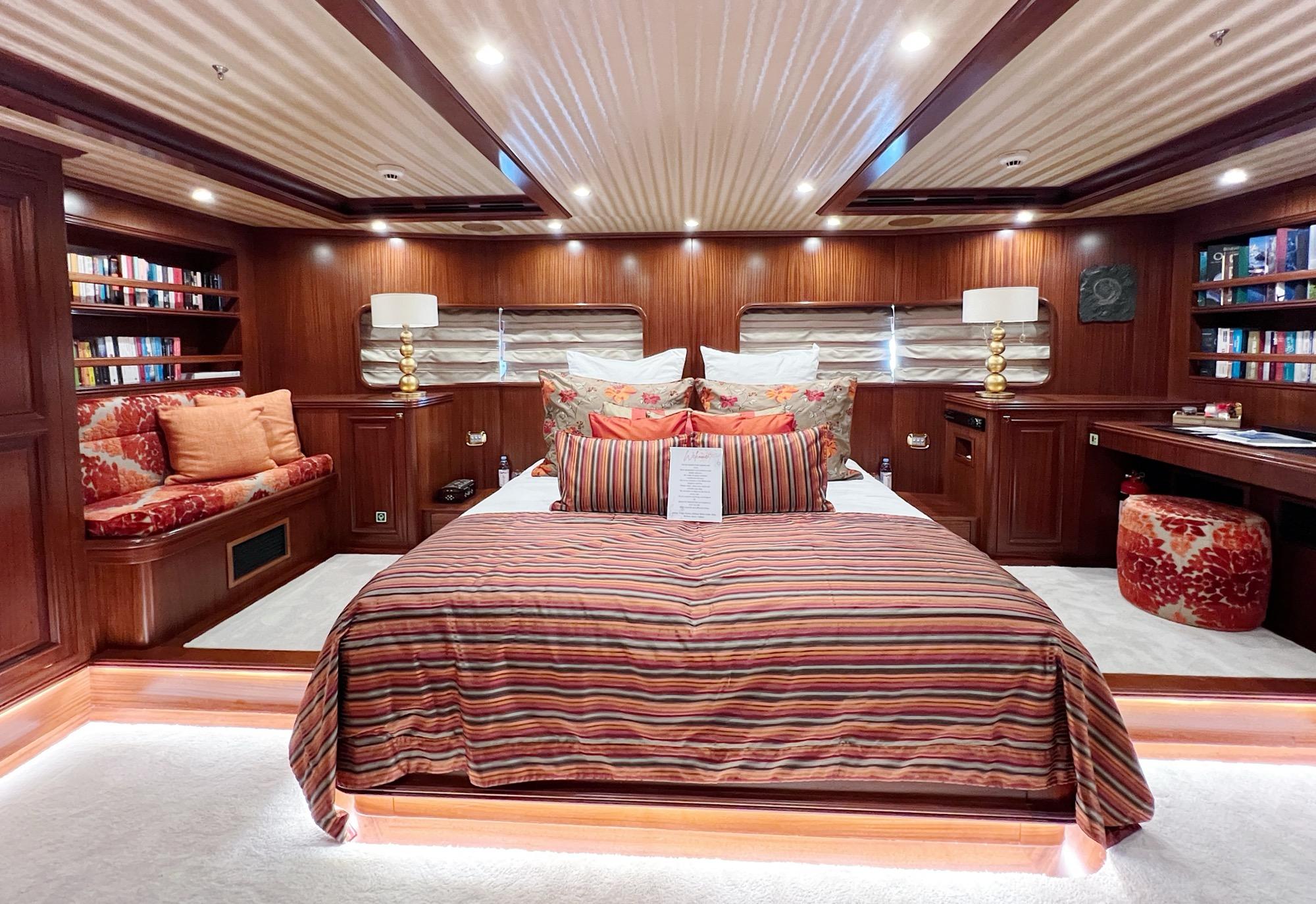 luxury yacht master cabin featuring king bed with striped bedding and extensive built-in library