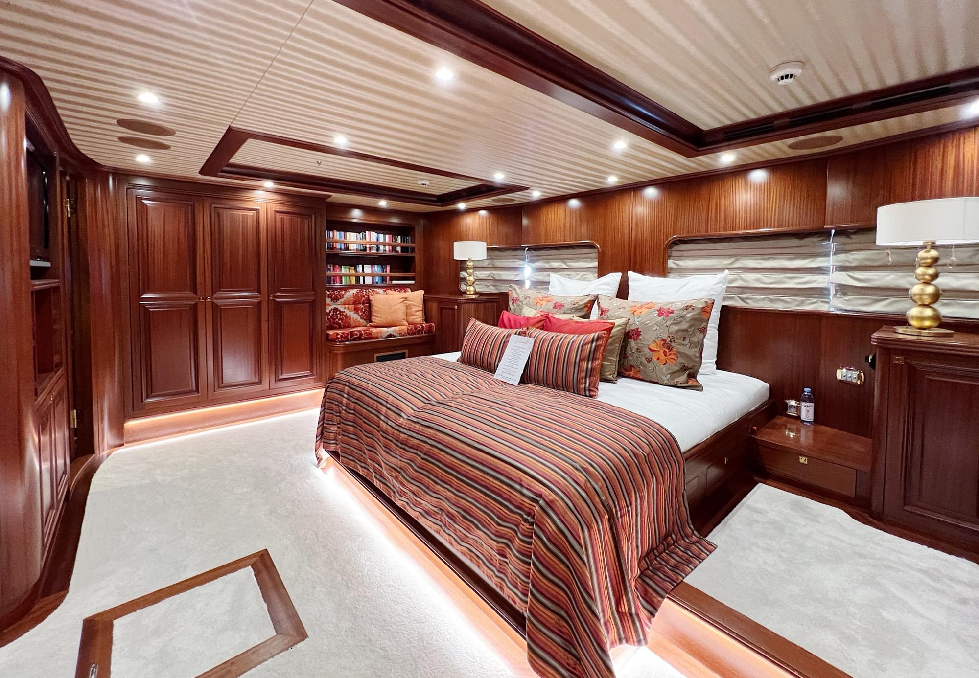 luxury yacht master cabin featuring king bed with striped bedding and built-in bookshelf