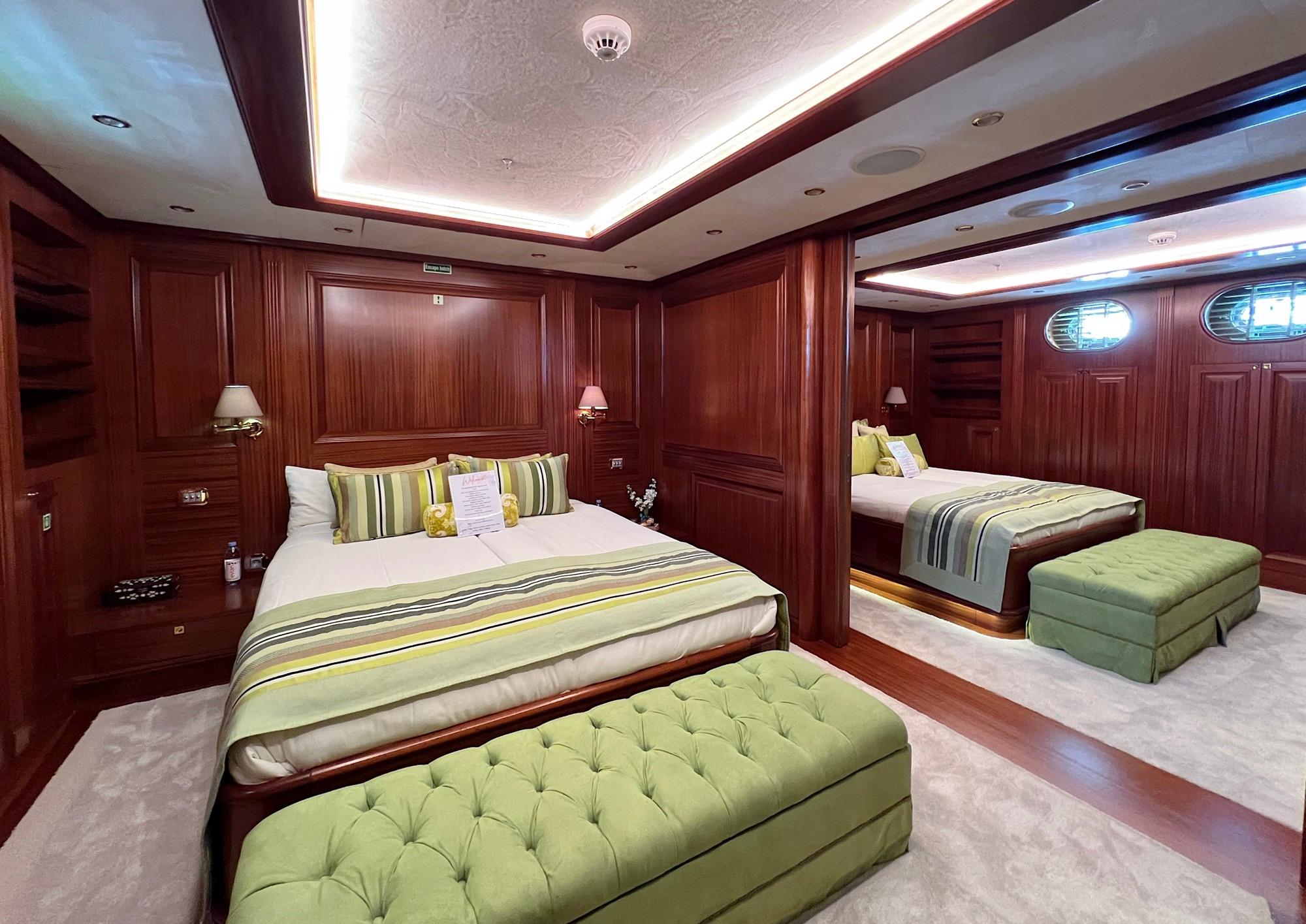 twin guest cabin with mahogany wood paneling, green striped bedding and tufted bench seating