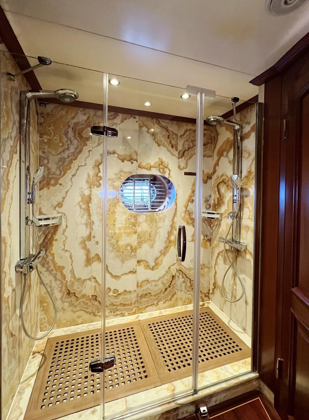 Spacious yacht shower with glass doors, marble walls, dual rainfall showerheads and teak flooring