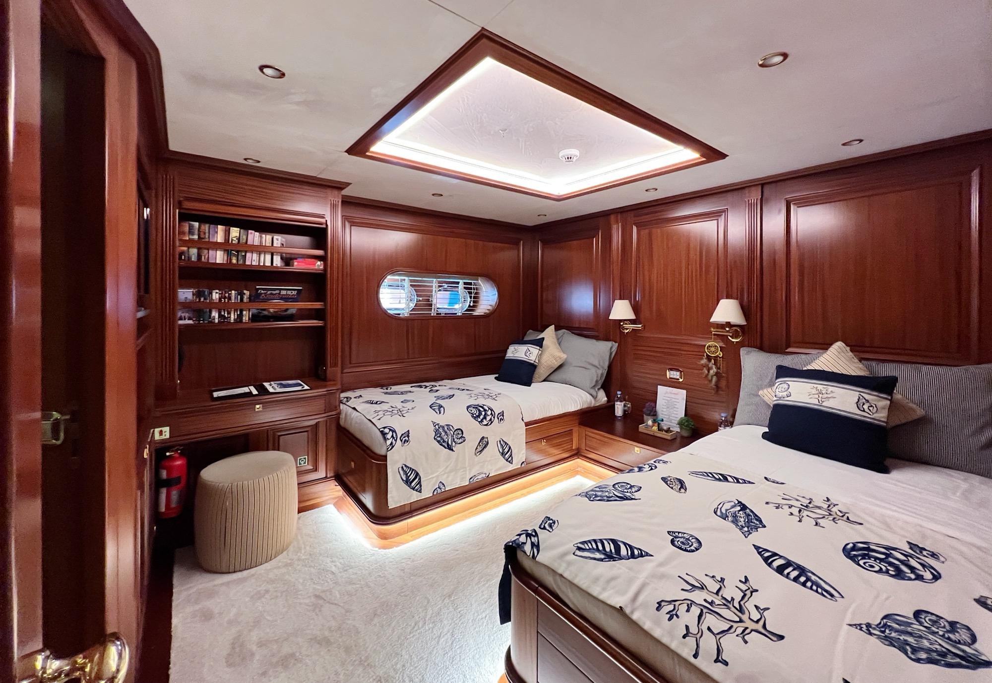 yacht twin cabin with two single beds, mahogany paneling, built-in bookshelf and oval porthole
