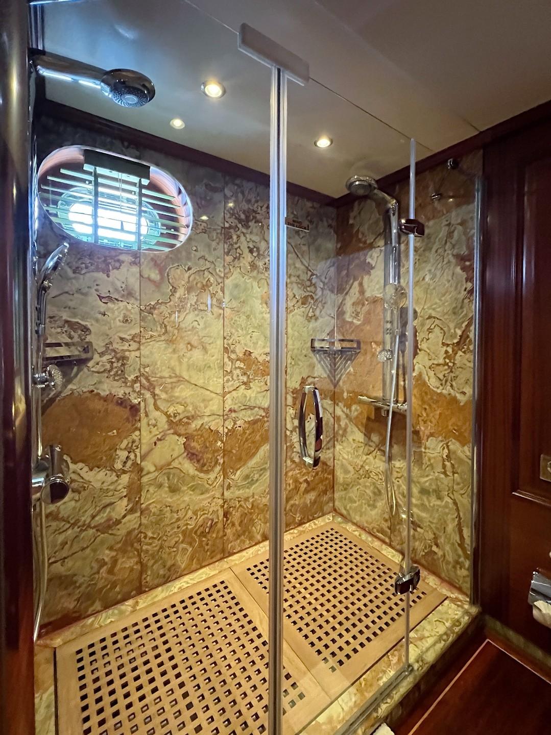 luxury yacht ensuite bathroom featuring marble-walled walk-in shower with glass doors and chrome fixtures